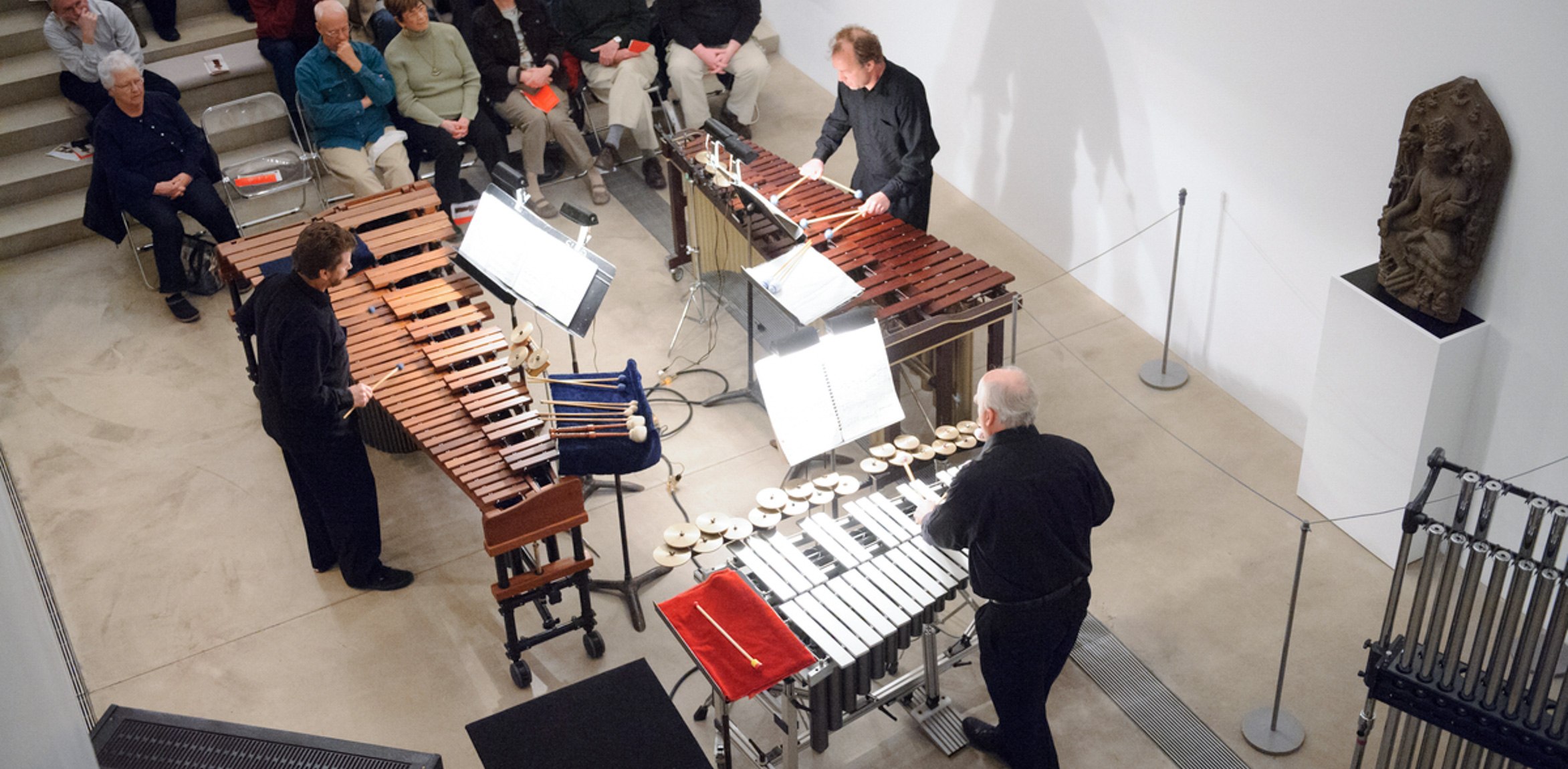 Three glockenspiel players perform for an audience in the Lower Main Gallery.