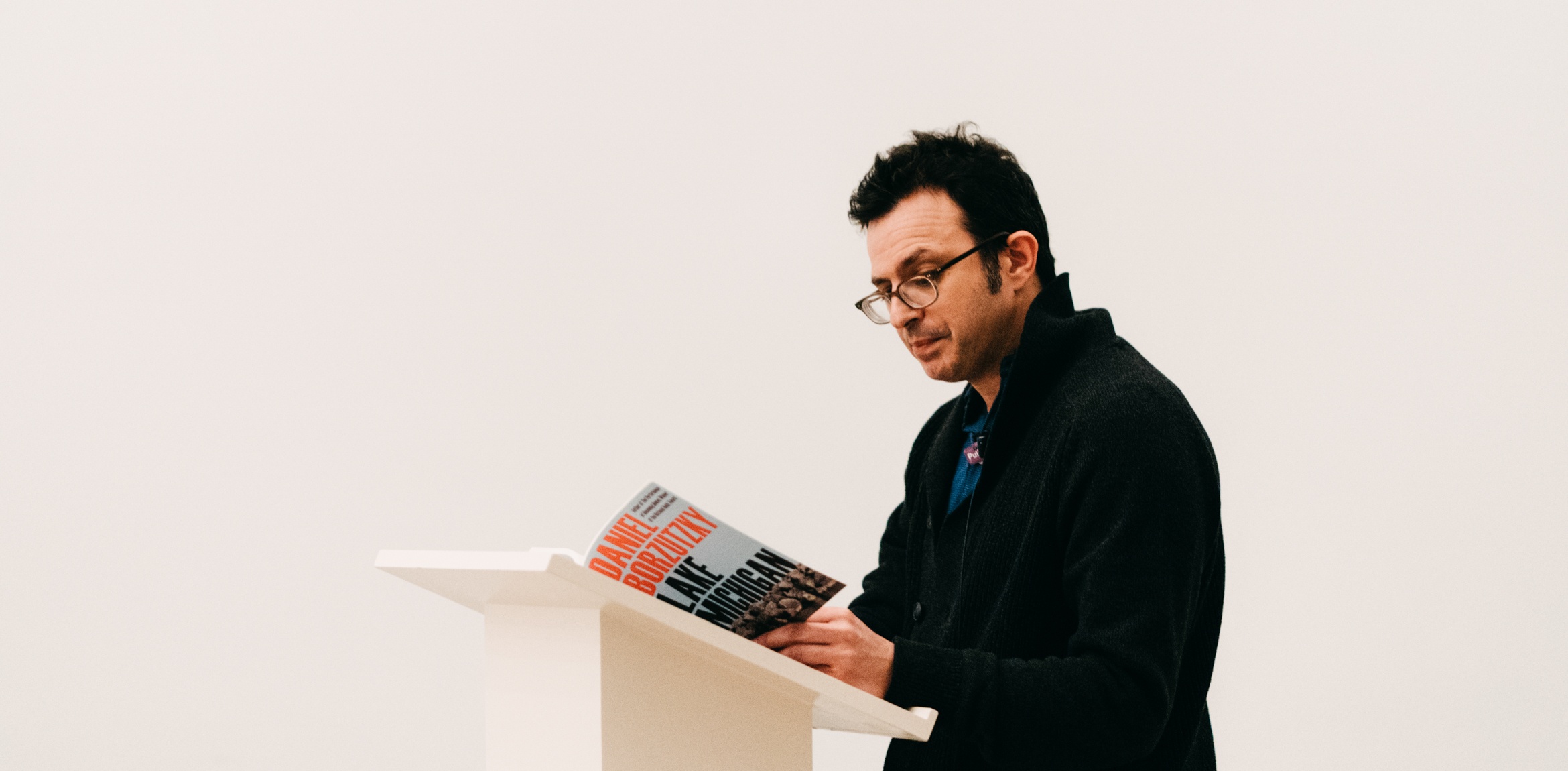 Poet Daniel Borzutzky reads from his collection at a white podium.
