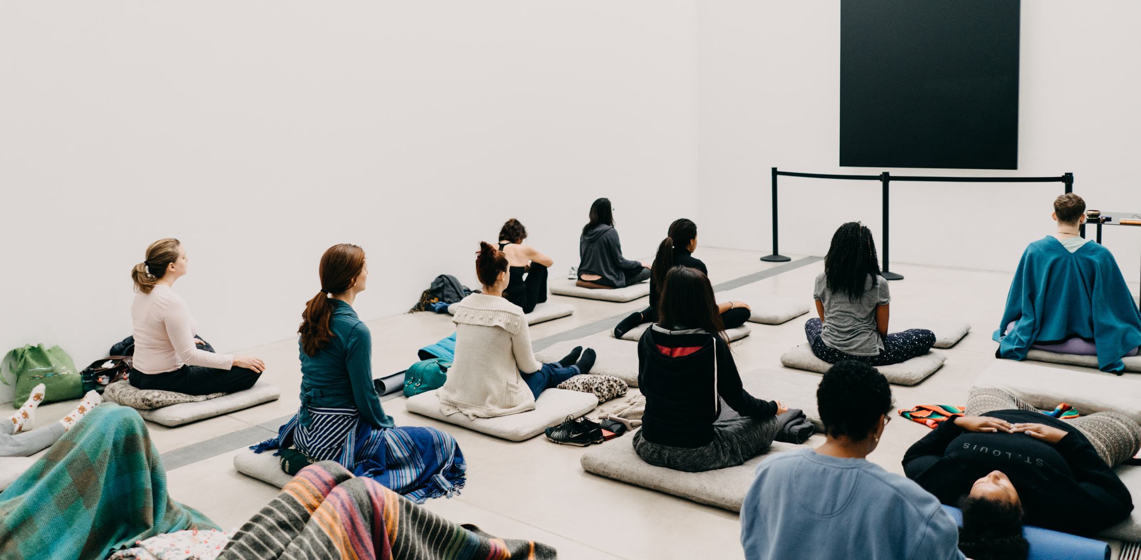 Guests sit on cushions in the Lower Main Gallery in meditative poses, facing Ellsworth Kelly's 