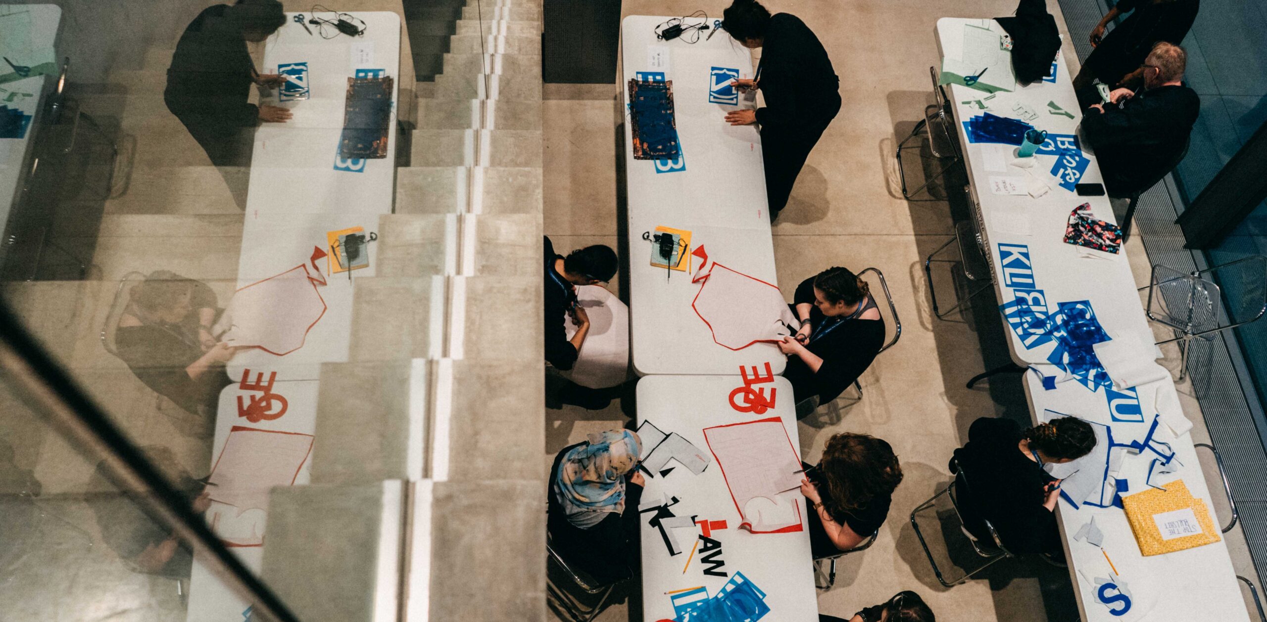 An aerial view of participants creating banners on long tables by the Water Court windows.