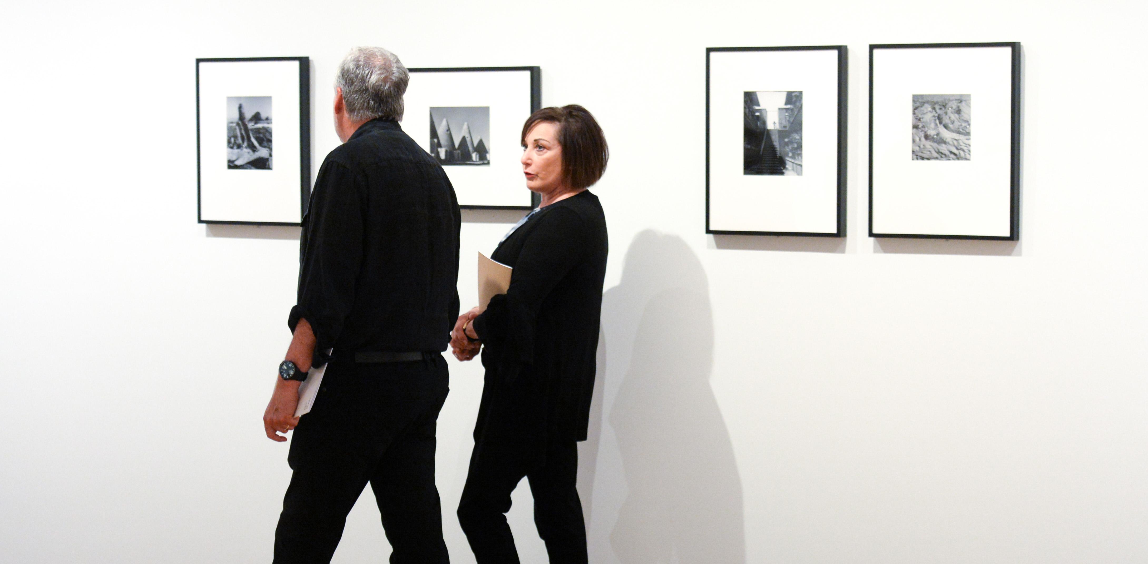 Two visitors walk past four framed black and white photographs by Lola Álvarez Bravo.