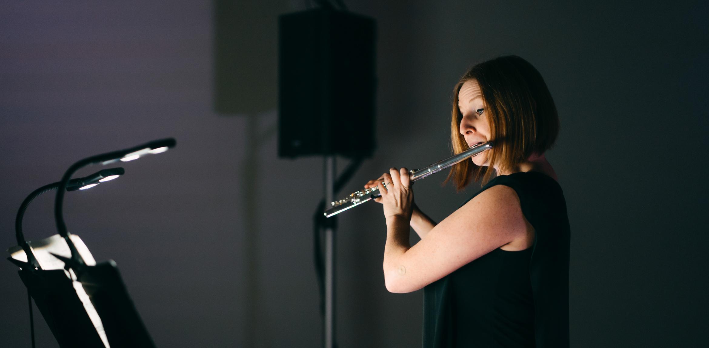 A flautist performs, lit by a music stand light.