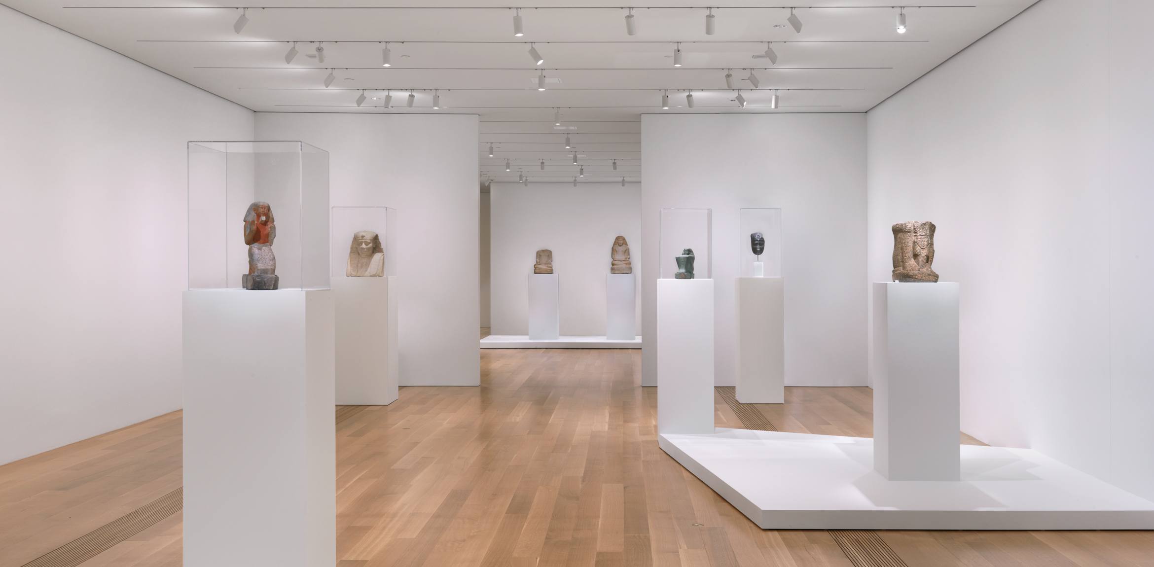 A view of Egyptian artifacts and sculptures on pedestals and vitrines in the Lower East Gallery.