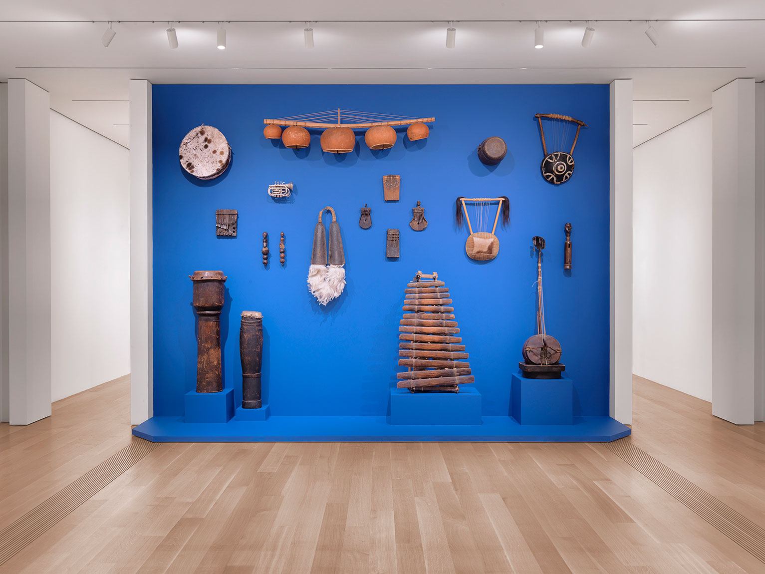 An exhibition view of Terry Adkins' collection of musical instruments, installed against a royal blue wall in the Lower East Gallery.