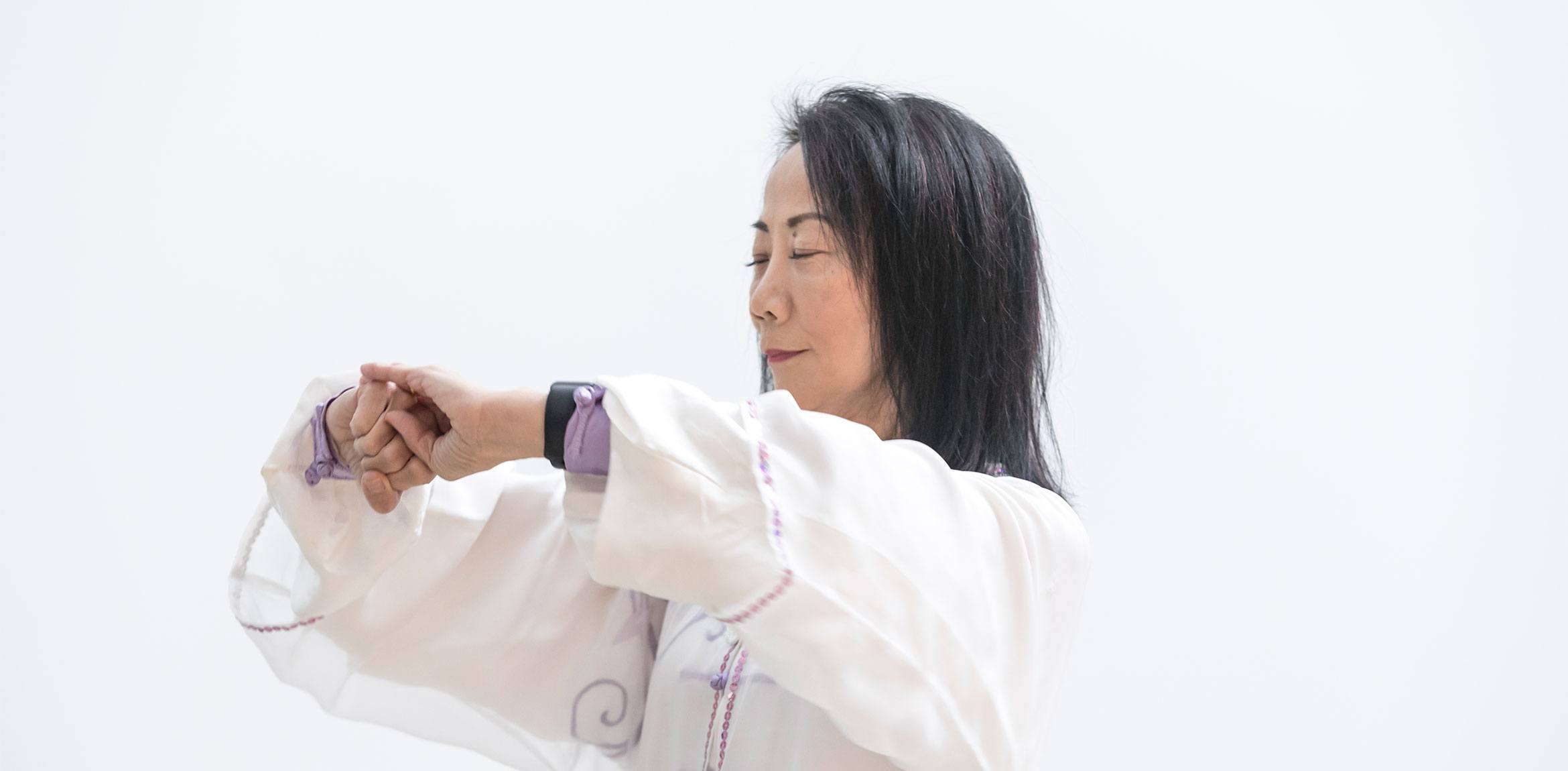 A closeup of Tai Chi Master Violet Li, standing with her eyes closed and her hands brought together in front of her chest.