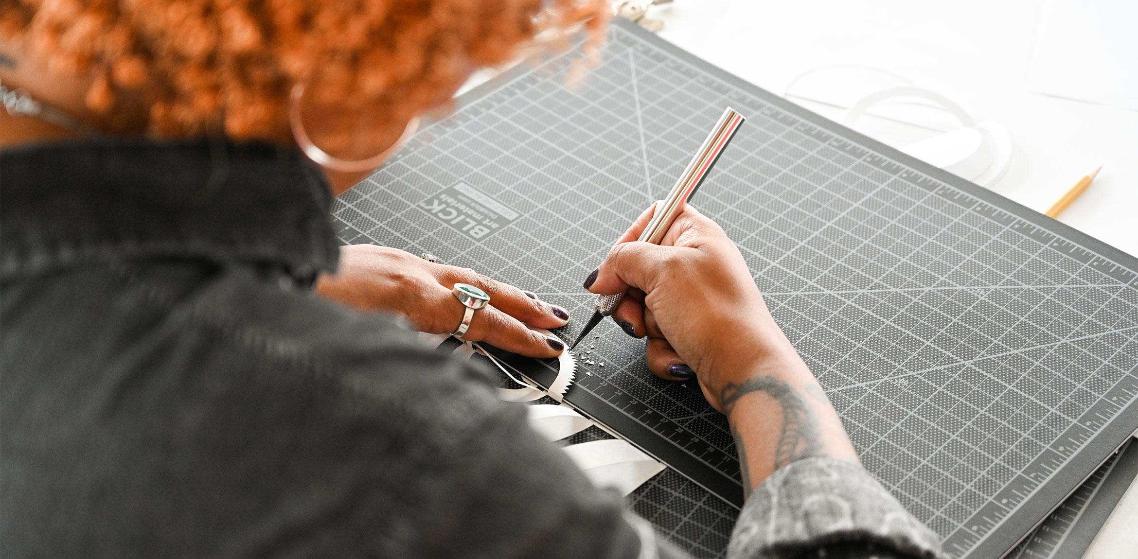 A closeup of a participant using an X-Acto knife to create a textured edge on a paper cut design.