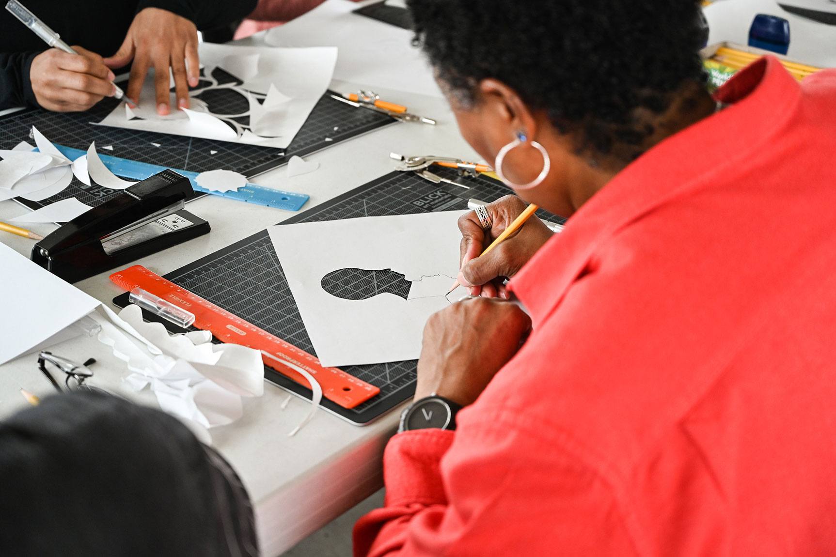 A closeup of participants sketching and cutting out designs on paper.