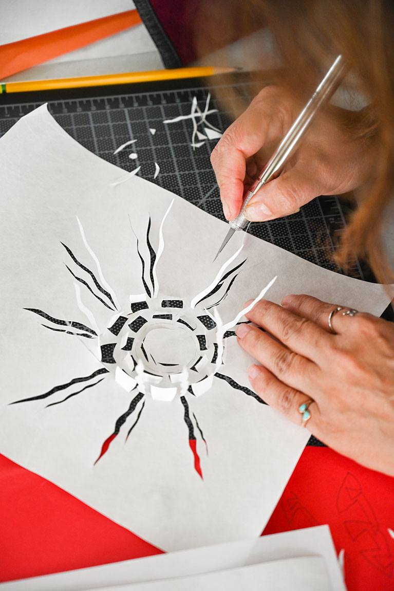 A closeup of a participant using an X-Acto knife to cut a sun design out of a piece of paper.