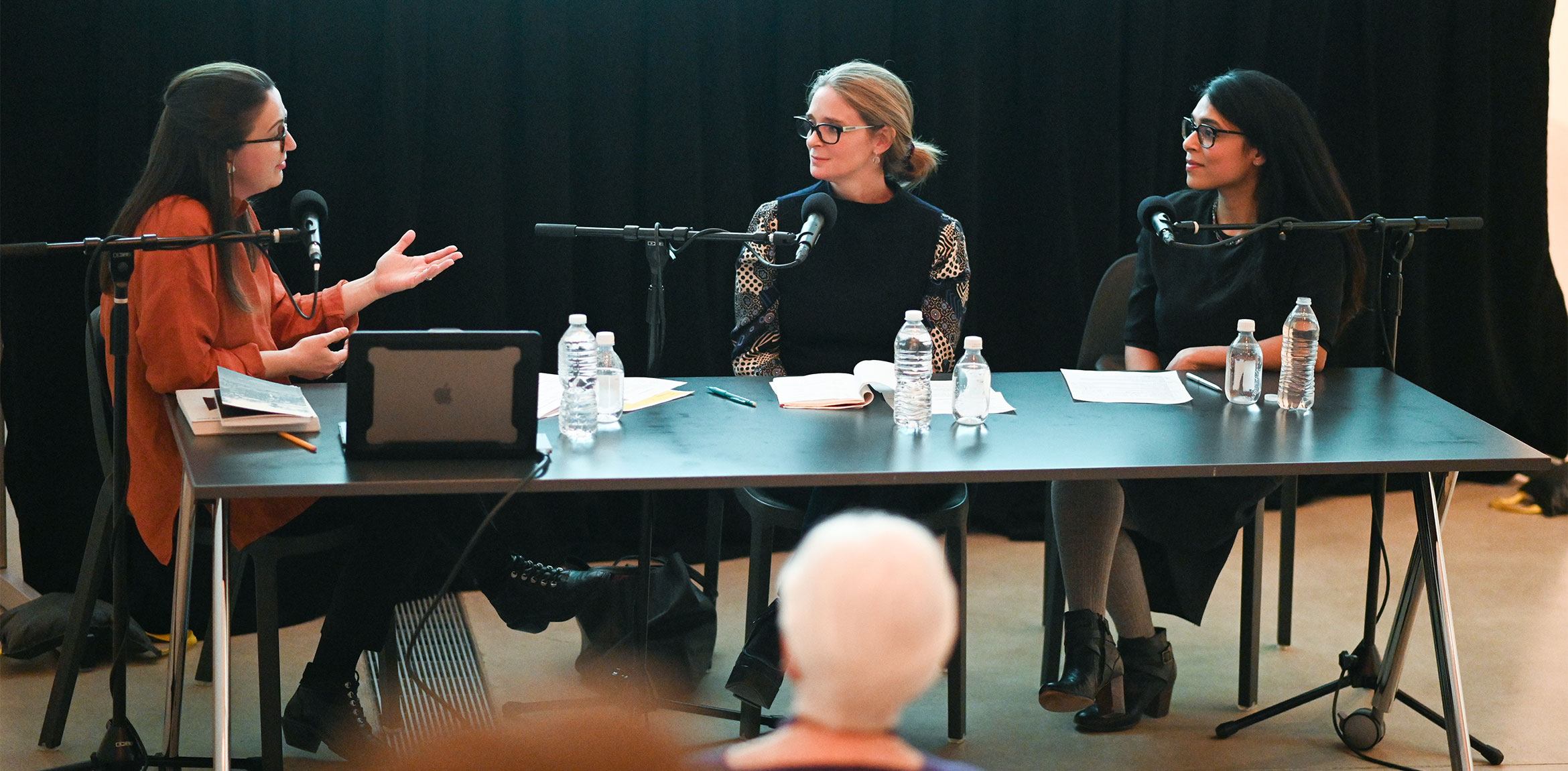 Tamara H. Schenkenberg speaks to Allegra Pesenti and Sarah Burney at a table with microphones in the Lower Main Gallery.