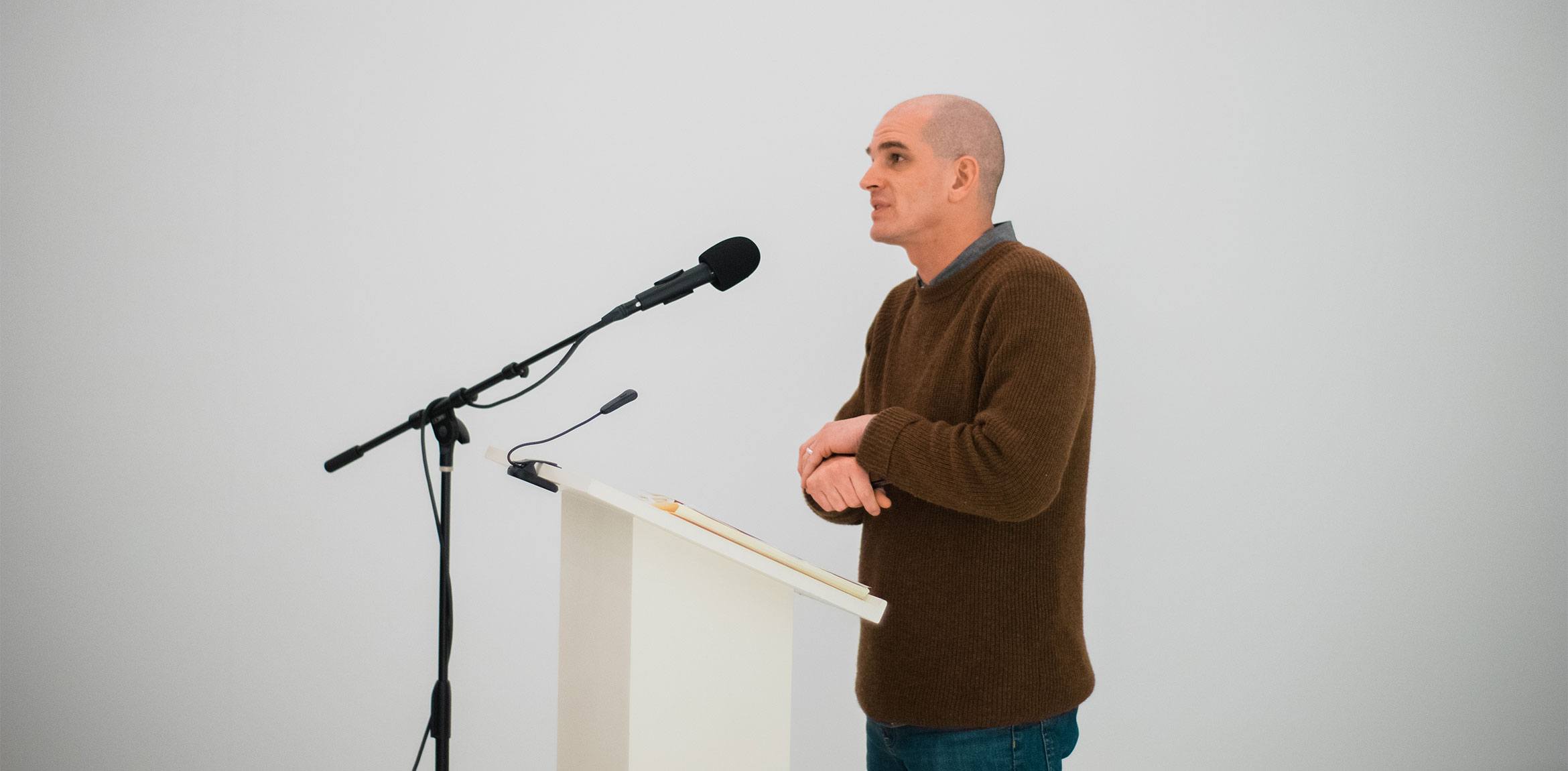 Ted Mathys speaks into a microphone behind a podium in the Lower Main Gallery.