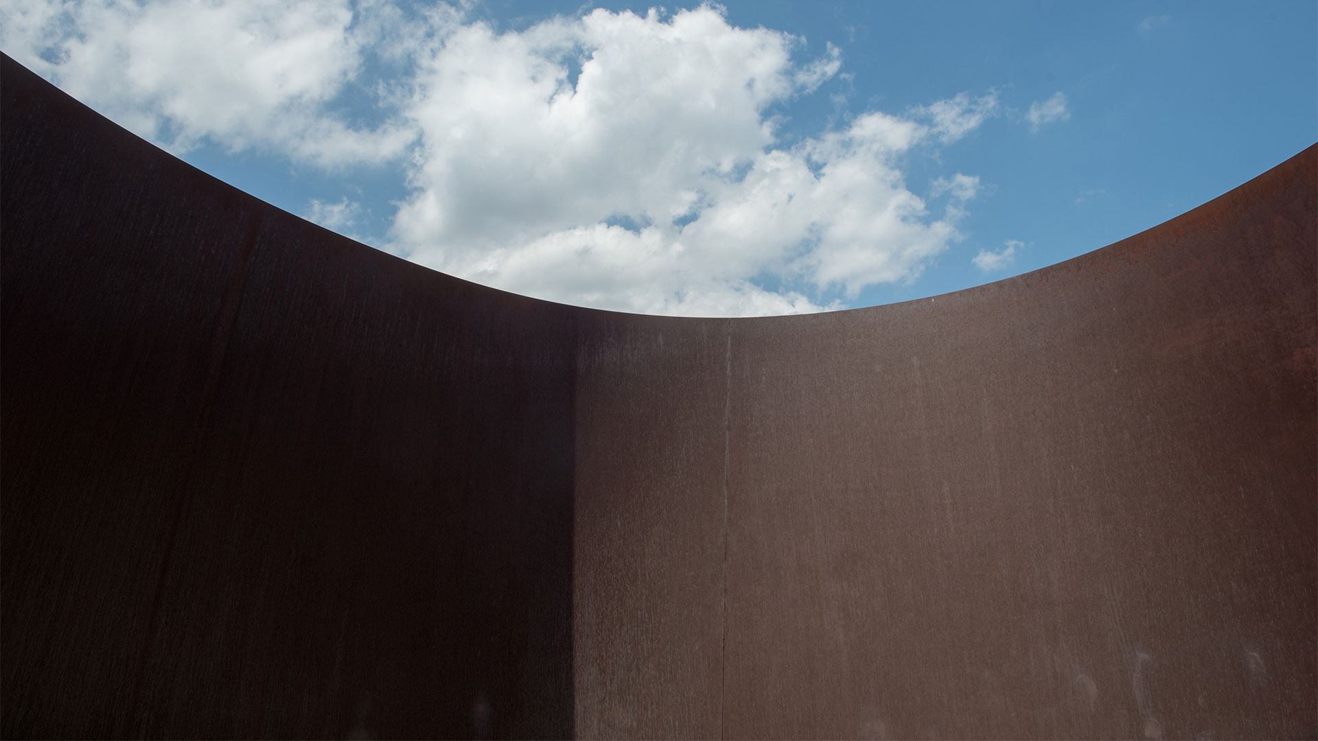 A blue cloudy sky outlined by the center spiral of Richard Serra's "Joe."