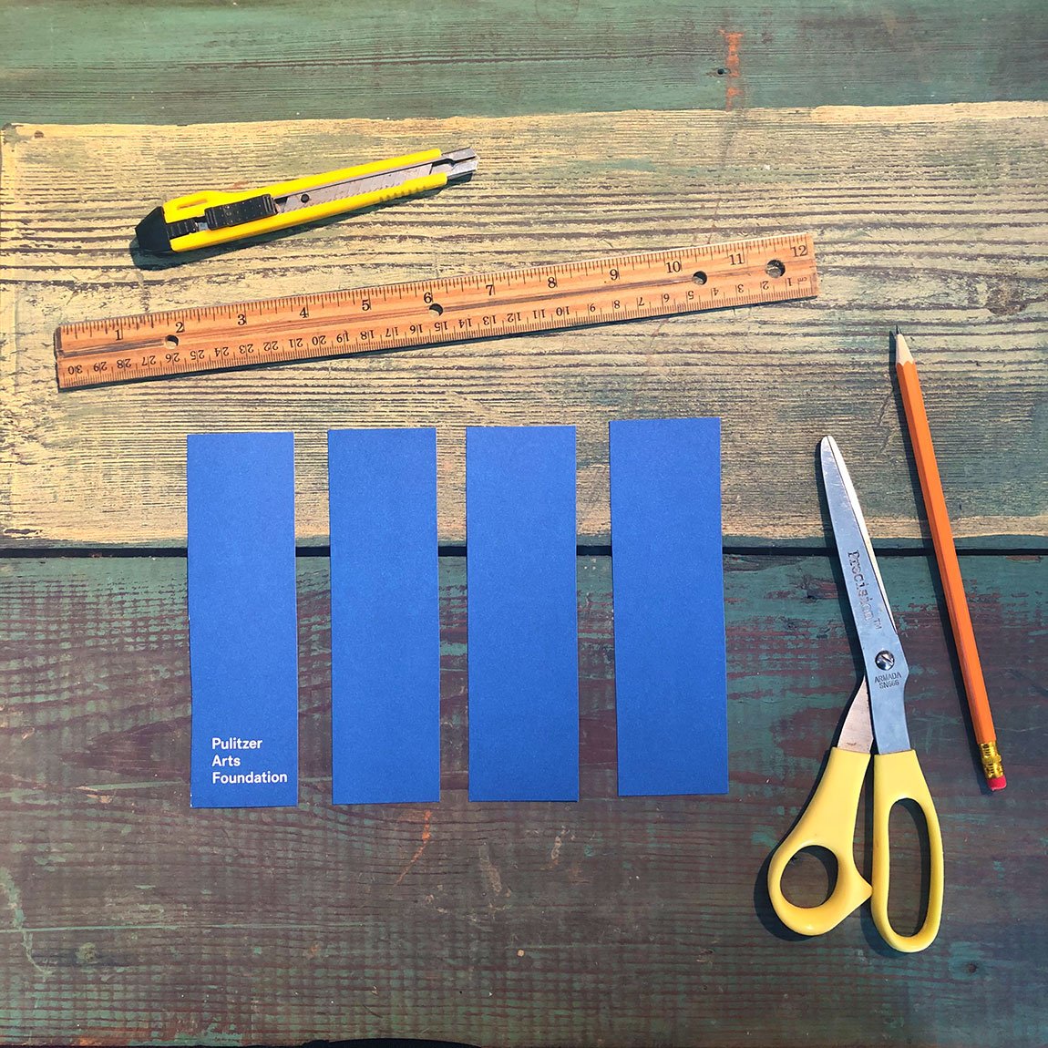 Four strips of a blue Pulitzer catalogue set on a wooden surface surrounded by tools.