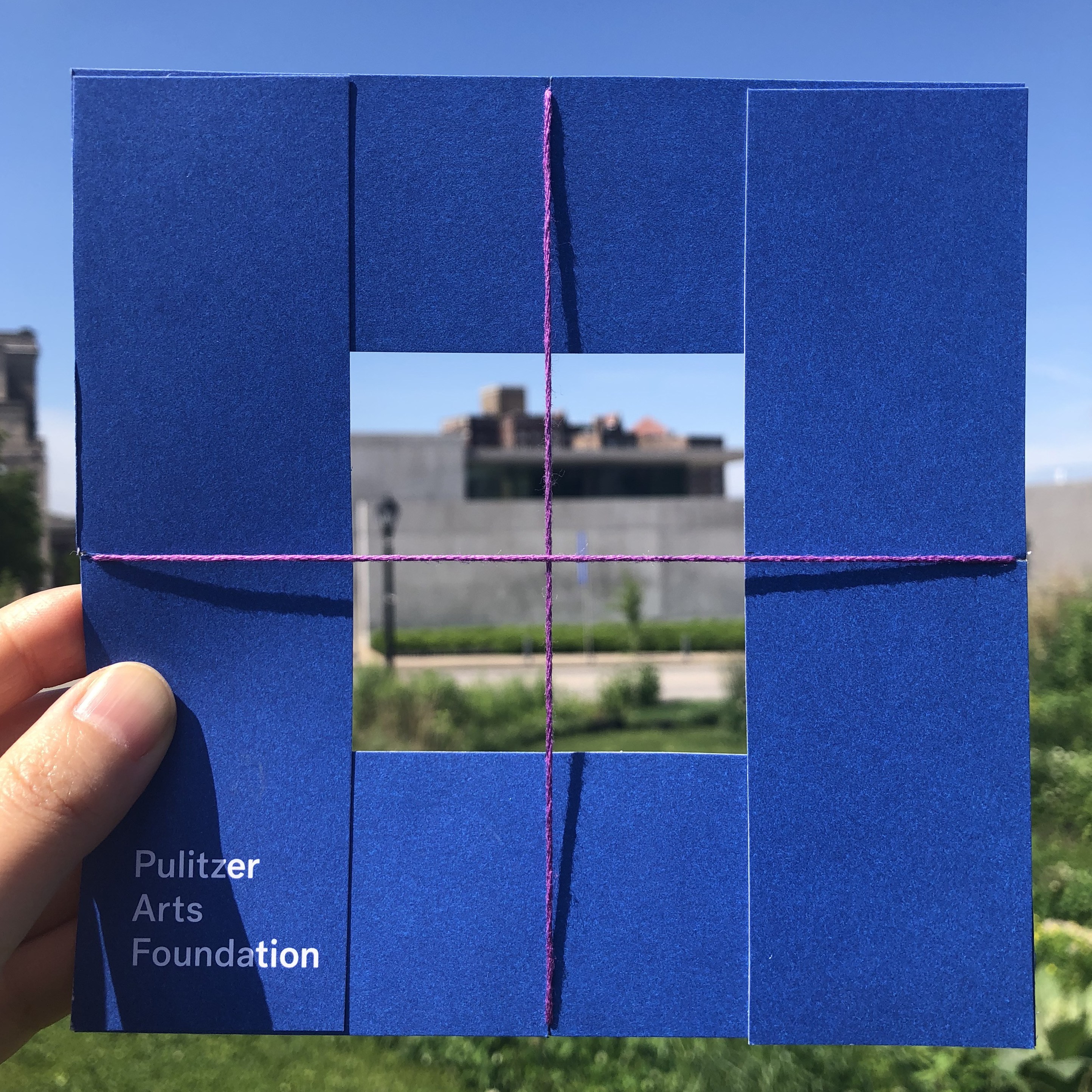A handmade square viewfinder, made with a blue Pulitzer catalogue and string, framing the Ando building.