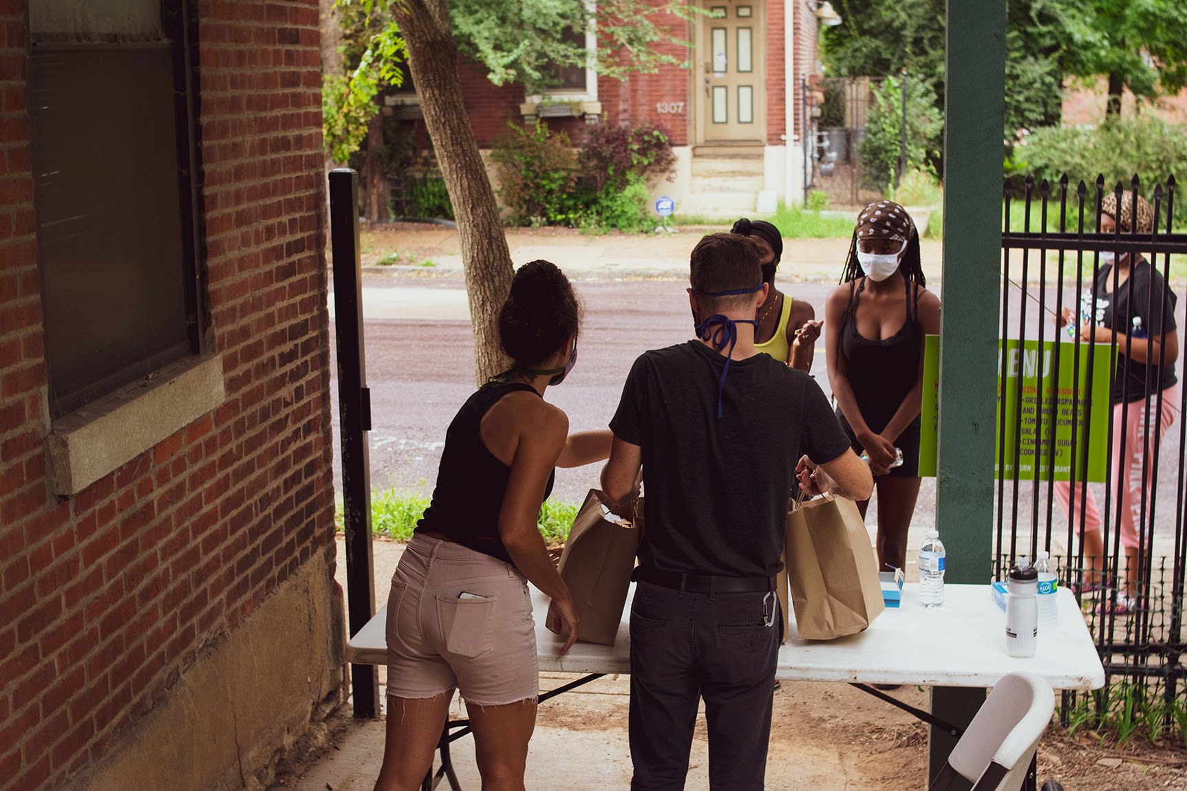 Volunteers distribute brown paper bags filled with food to community members at the Northside Workshop entrance.