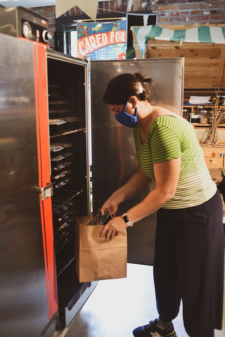 A volunteer fills a brown paper bag with food supplies from a fridge.