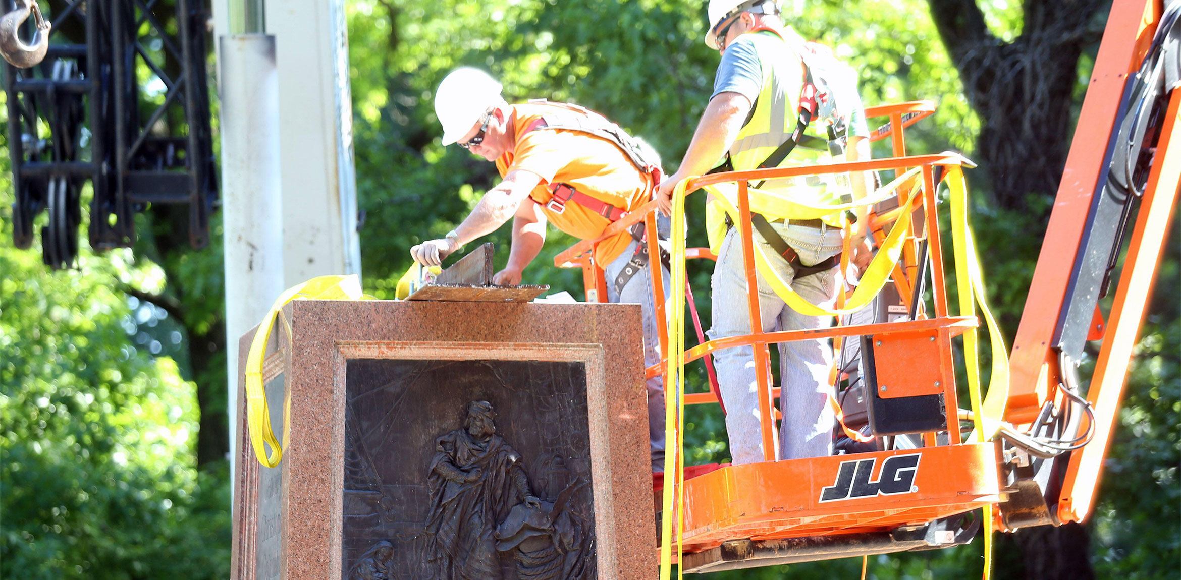 Two construction workers in a man lift remove the base of the Christopher Columbus statue in Tower Grove Park.