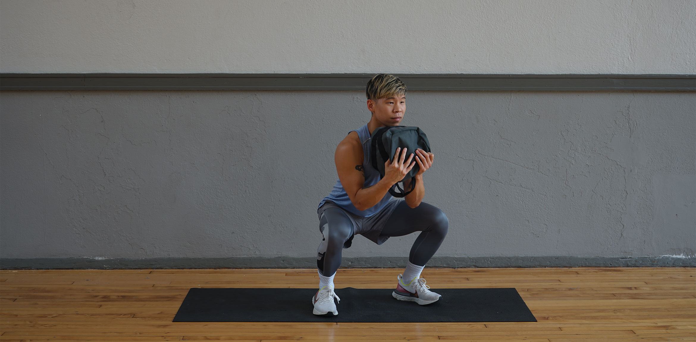 Yowshien Kuo squats on a yoga mat, holding a sandbag to his chest.