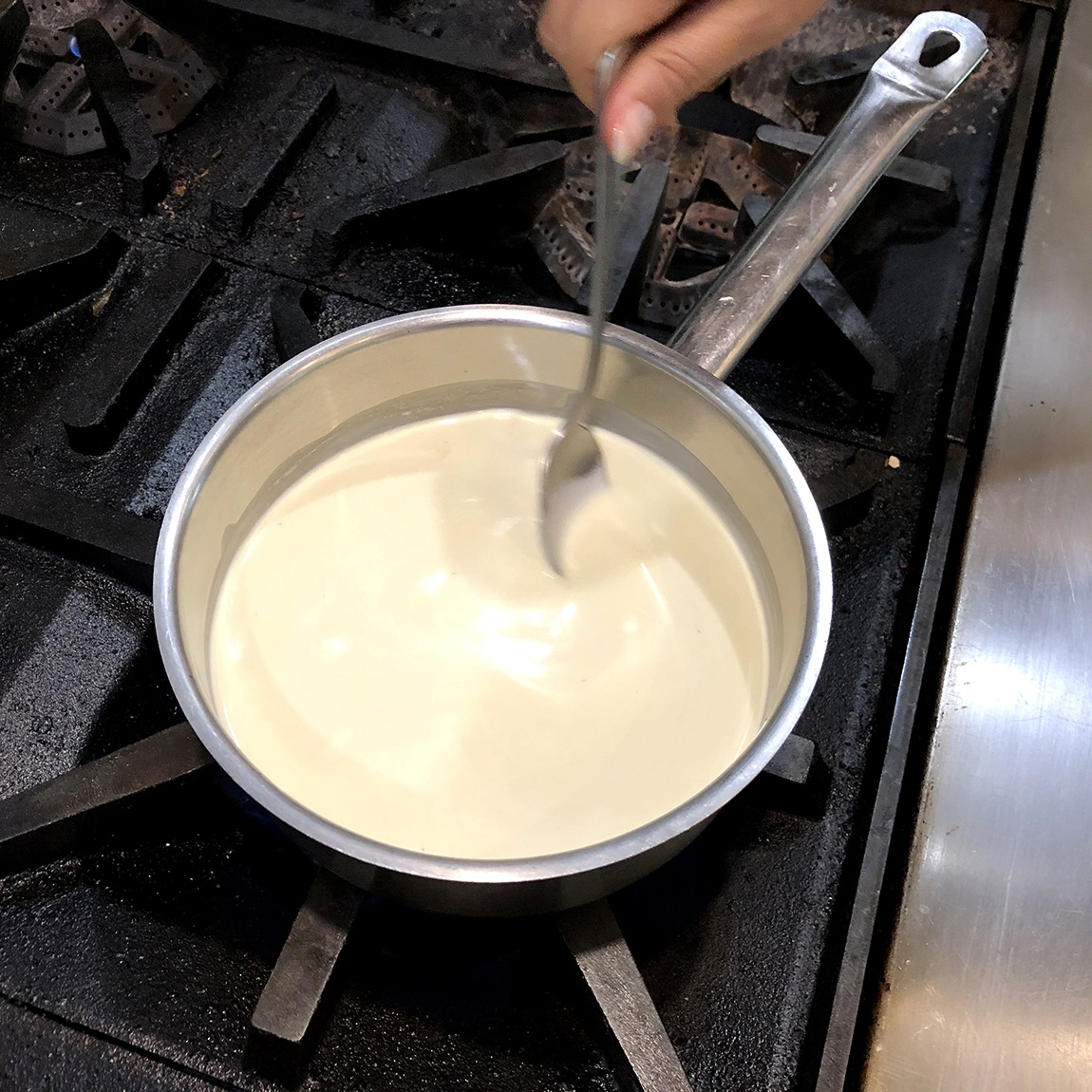 Summer Wright mixes a creamy substance in a metal saucepan on a stovetop.