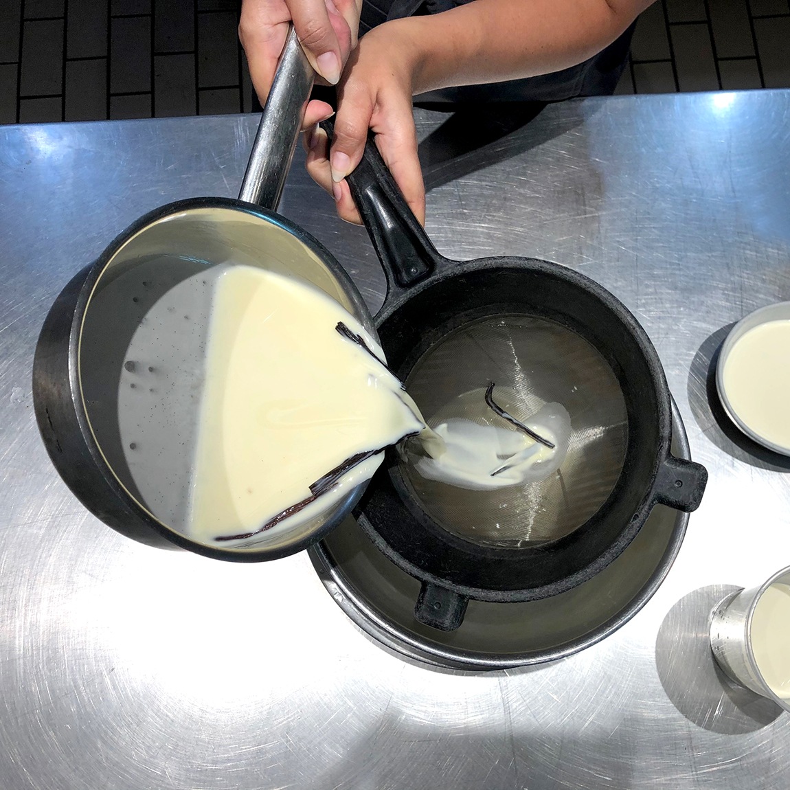 Summer Wright pours vanilla pudding into a strainer above a mixing bowl on a metal counter.