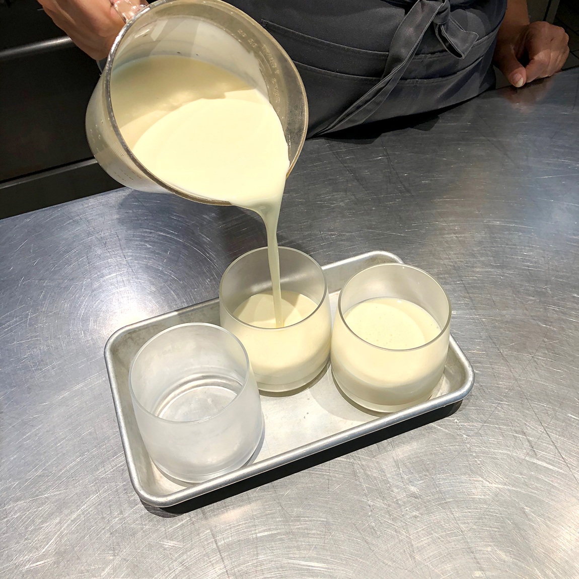 Summer Wright pours vanilla pudding into glass cups on a small baking tray.