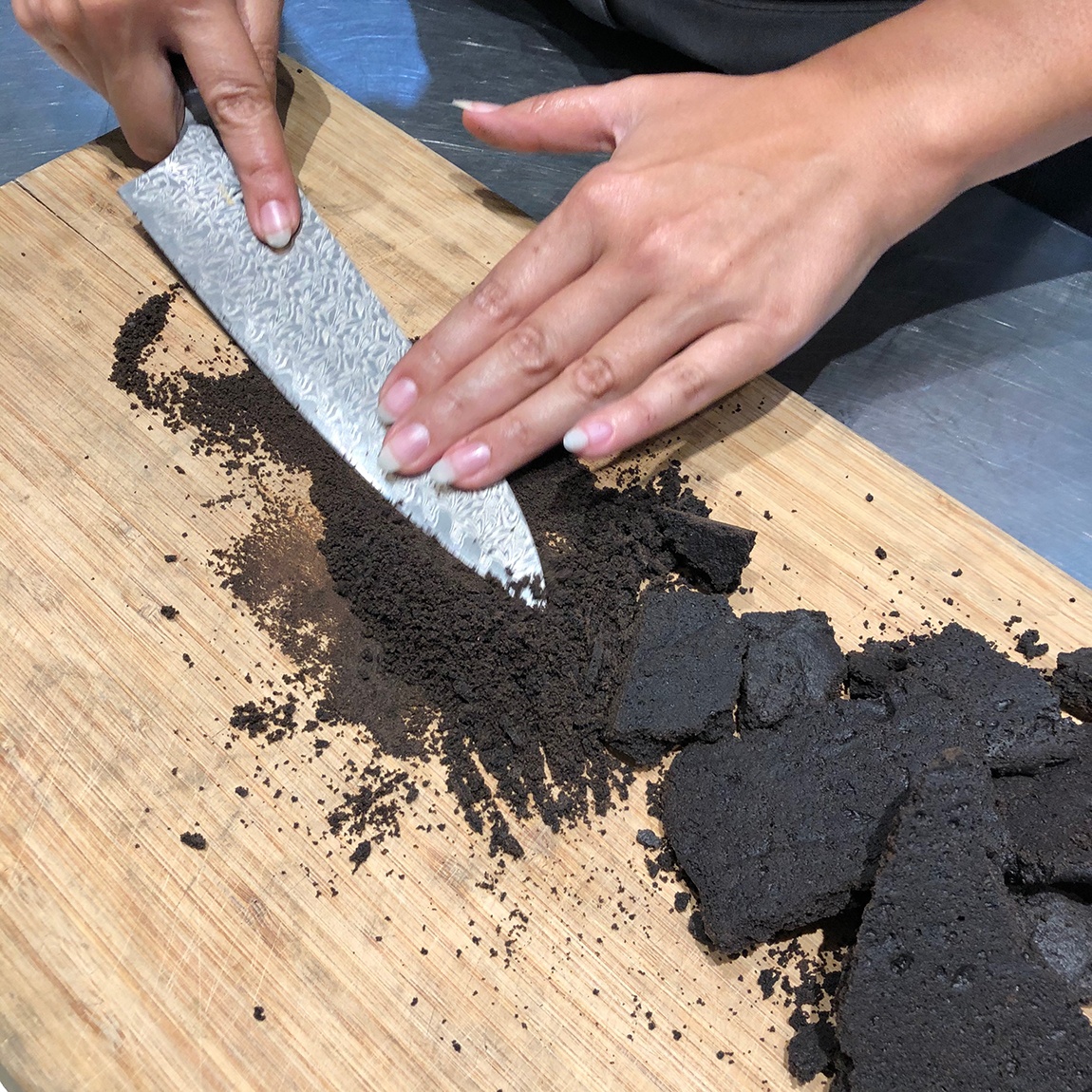 Summer Wright uses the flat side of a knife to crush chocolate wafers on a wood cutting board.