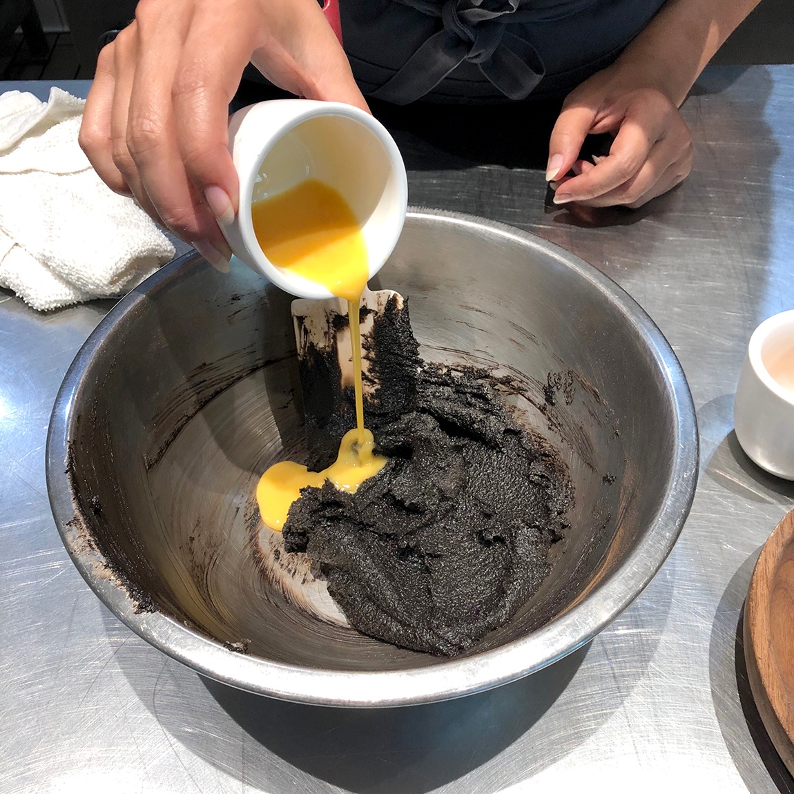 Summer Wright pours an egg yolk into a metal mixing bowl with a chocolate substance.