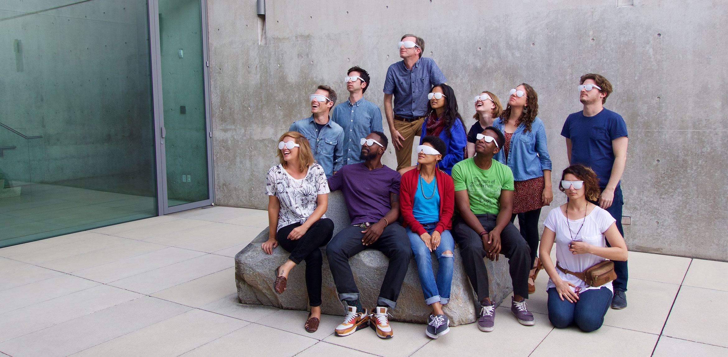 A group of workshop participants wearing listening glasses gathers around and on Scott Burton's "Rock Settee" in the Water Court.