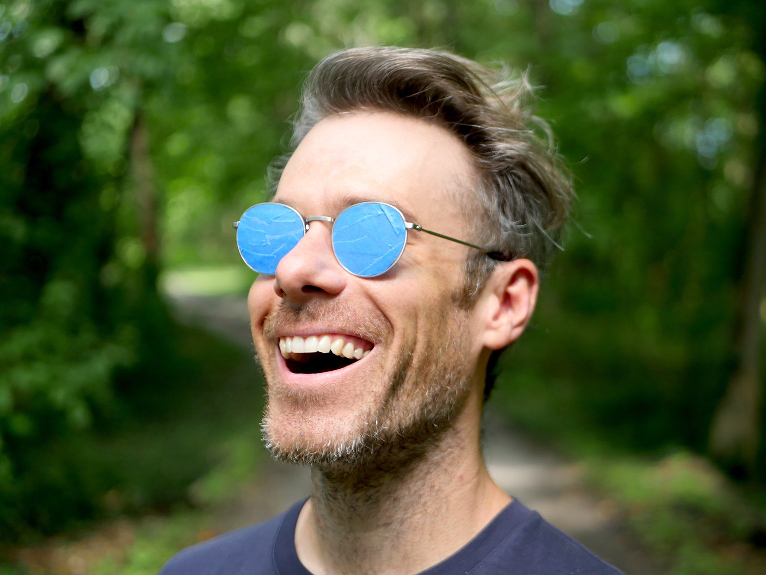 A portrait of Chris Kallmyer wearing listening glasses and smiling outdoors.