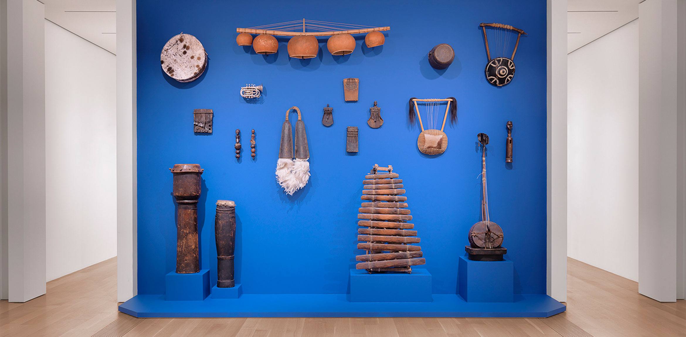 An exhibition view of Terry Adkins' collection of musical instruments, installed against a royal blue wall in the Lower East Gallery.