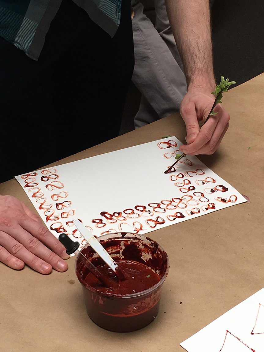 A participant draws infinity symbols on a page with a stem and natural pigment.