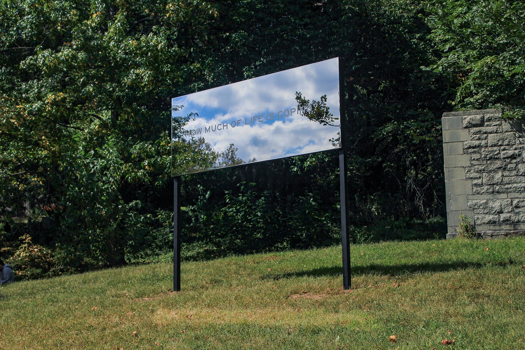 Chloë Bass' mirrored steel piece "How much of life is coping?" installed on a grass hill.