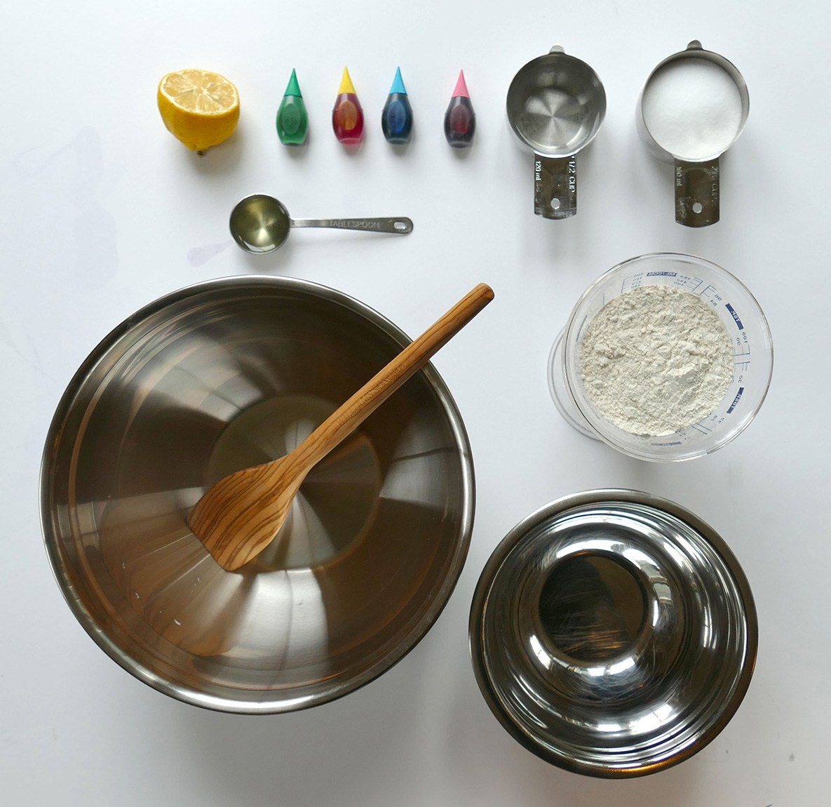 Clay making supplies—including two metal bowls, flour, salt, water, food coloring, and half a lemon—laid out on a table