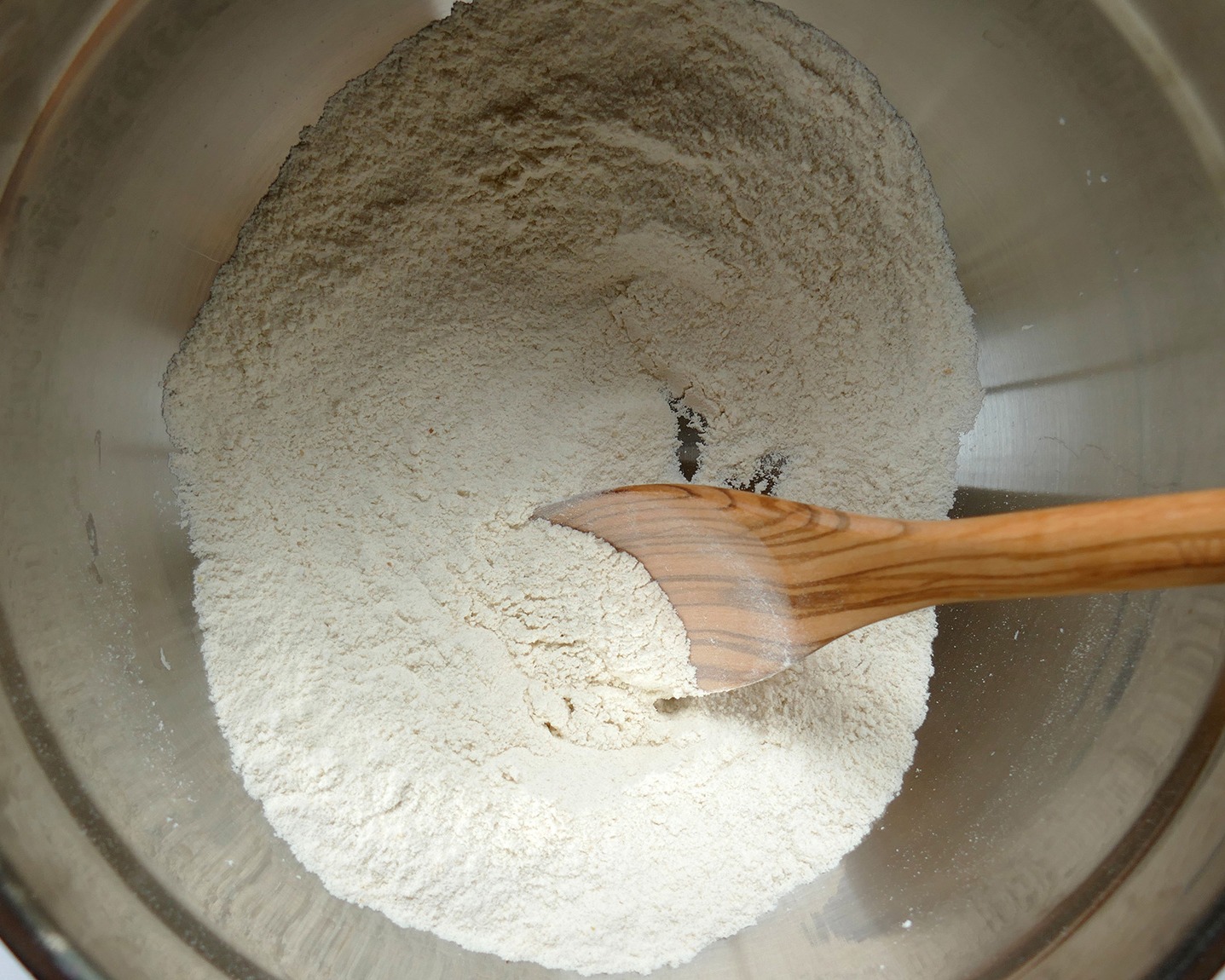 Dry ingredients mixed together in a metal bowl with a wooden spoon inserted in the mixture
