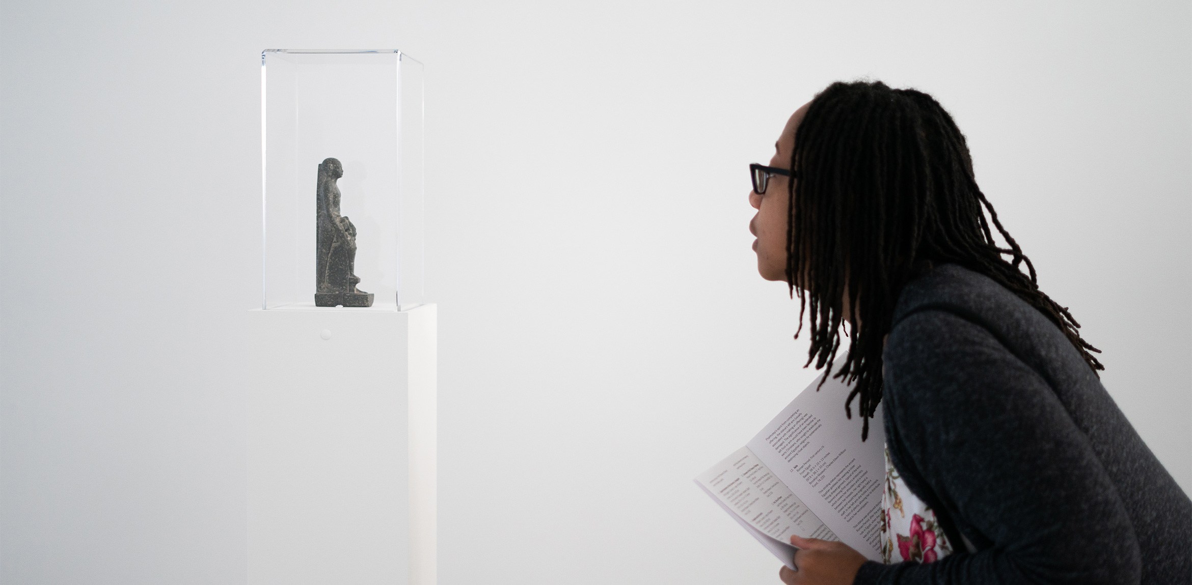Visitor leaning forward and looking at small ancient Egyptian figure inside of a slim vitrine