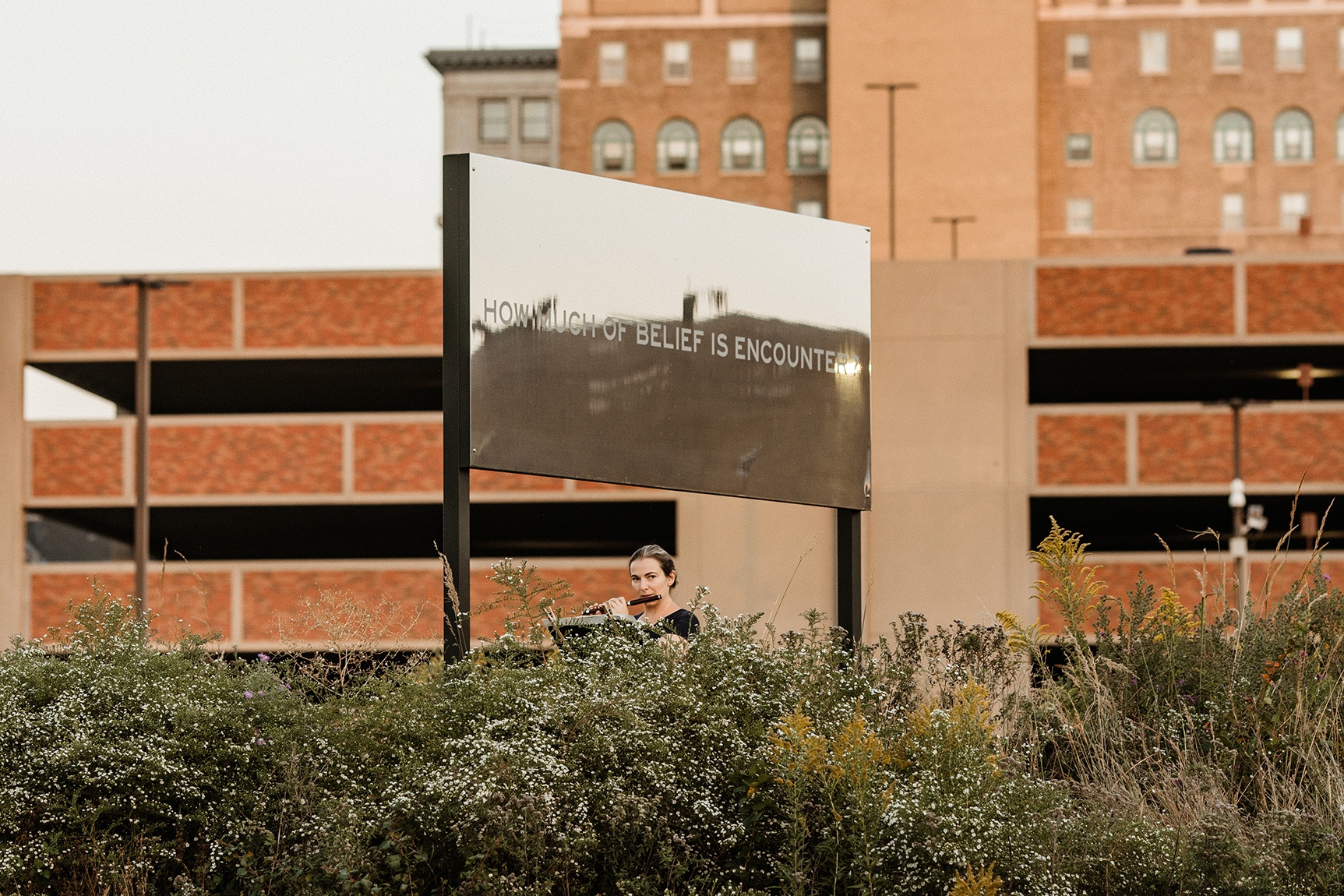 A St. Louis Symphony Orchestra musician performing outdoors in Park-Like while standing below a large billboard by artist Chloë Bass