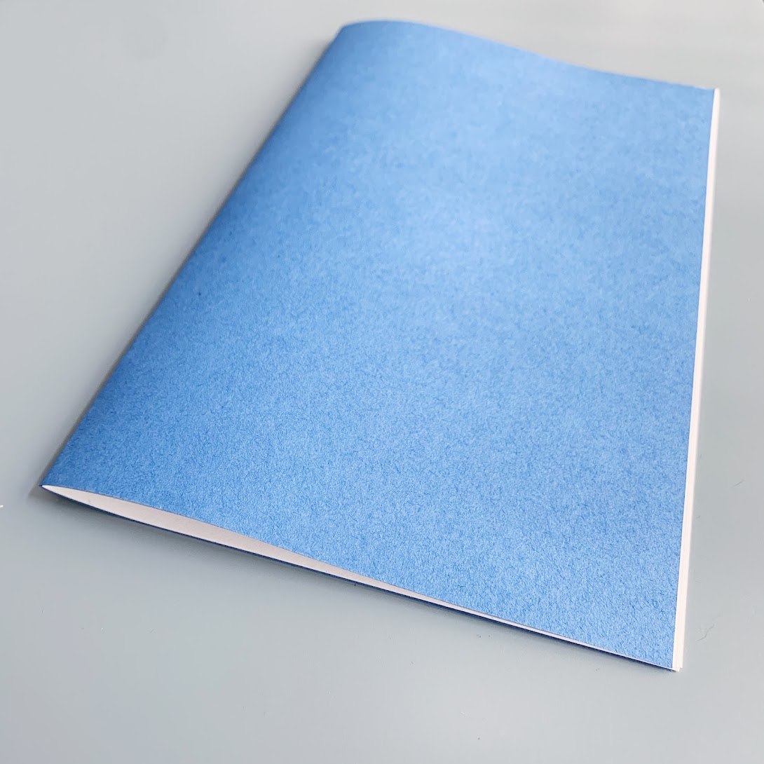 An in-progress zine with a blue cover folded over white pages
