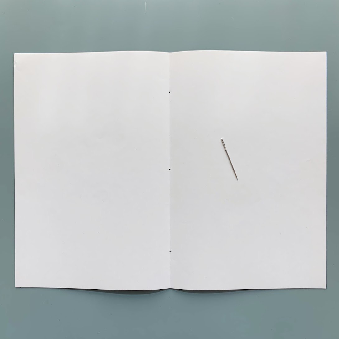 A needle resting on the folded pages of an in-progress zine