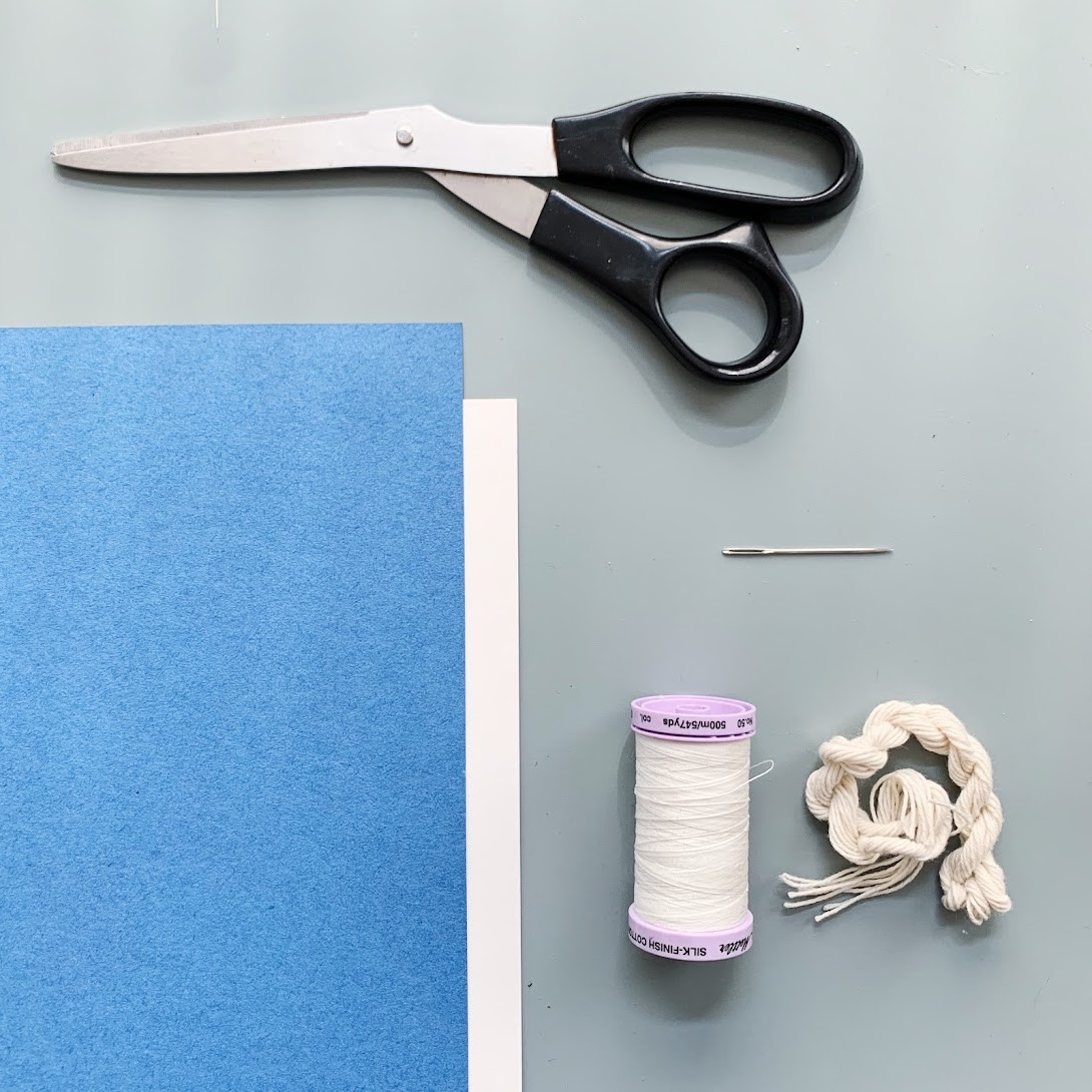 A pair of scissors, a needle, two types of thread, and blue and white paper