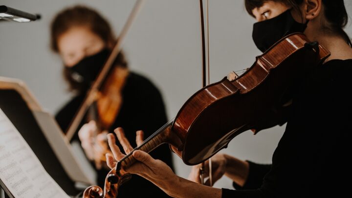 Close-up of a musician playing the violin. A second musician is visible in the background.