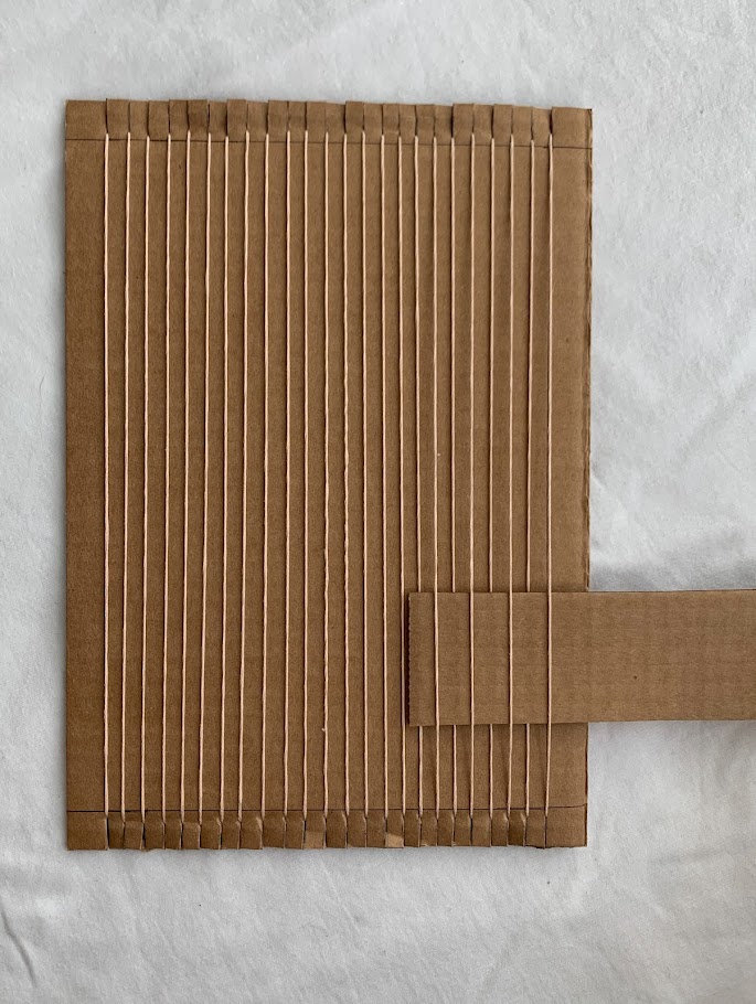 A cardboard scrap inserted into a strung cardboard loom