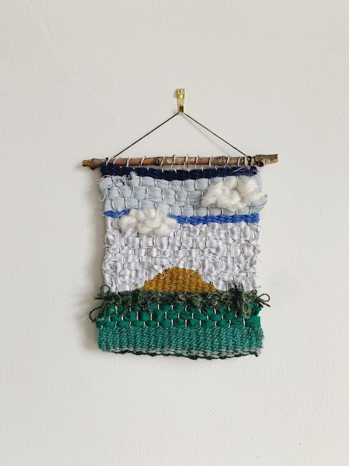A hung finished weaving depicting a skyline and clouds
