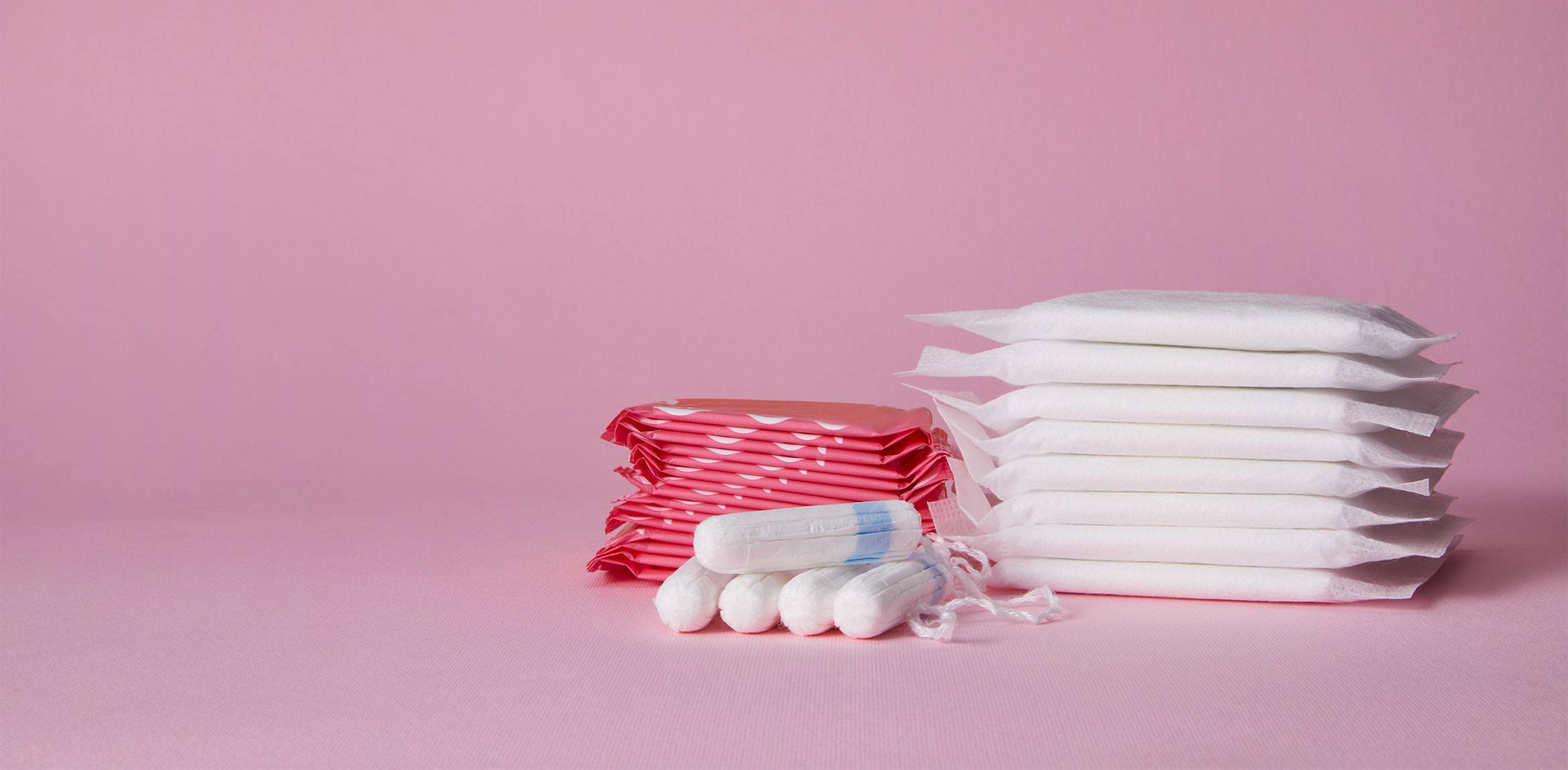 Stacks of menstrual pads and tampons on a pink background