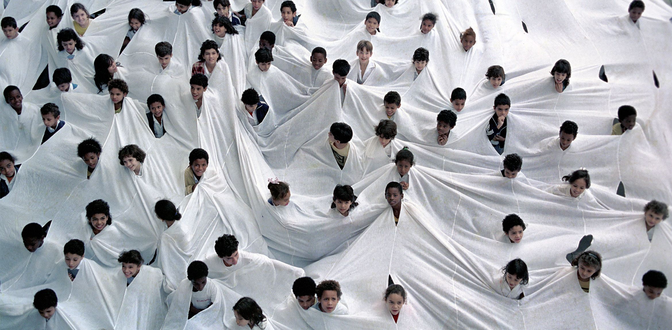Documentation of a public performance by Lygia Pape involving hundreds of children wearing a large white textile