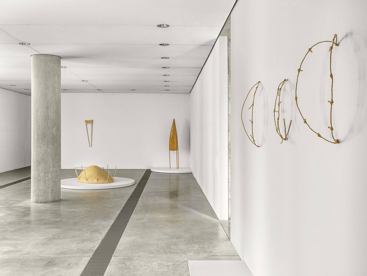 Installation view of Faye HeavyShield's work, including three yellow wired ochre traps on the wall to the right, a cone shaped paper mache sculpture and a sculpture in the form of a pregnant belly with spikes coming out, on the gallery floor.