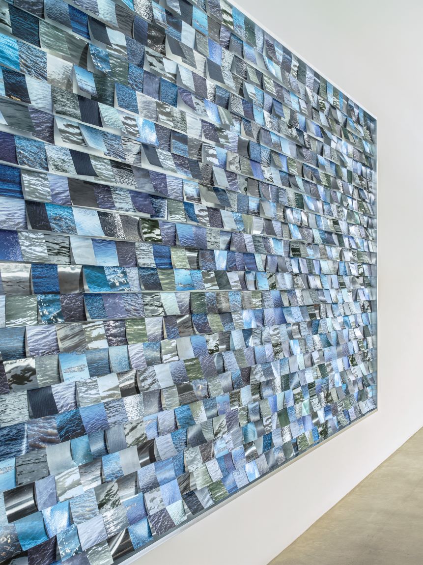 Close up of wall installation with thousands of blue and green photographs of various different rivers.