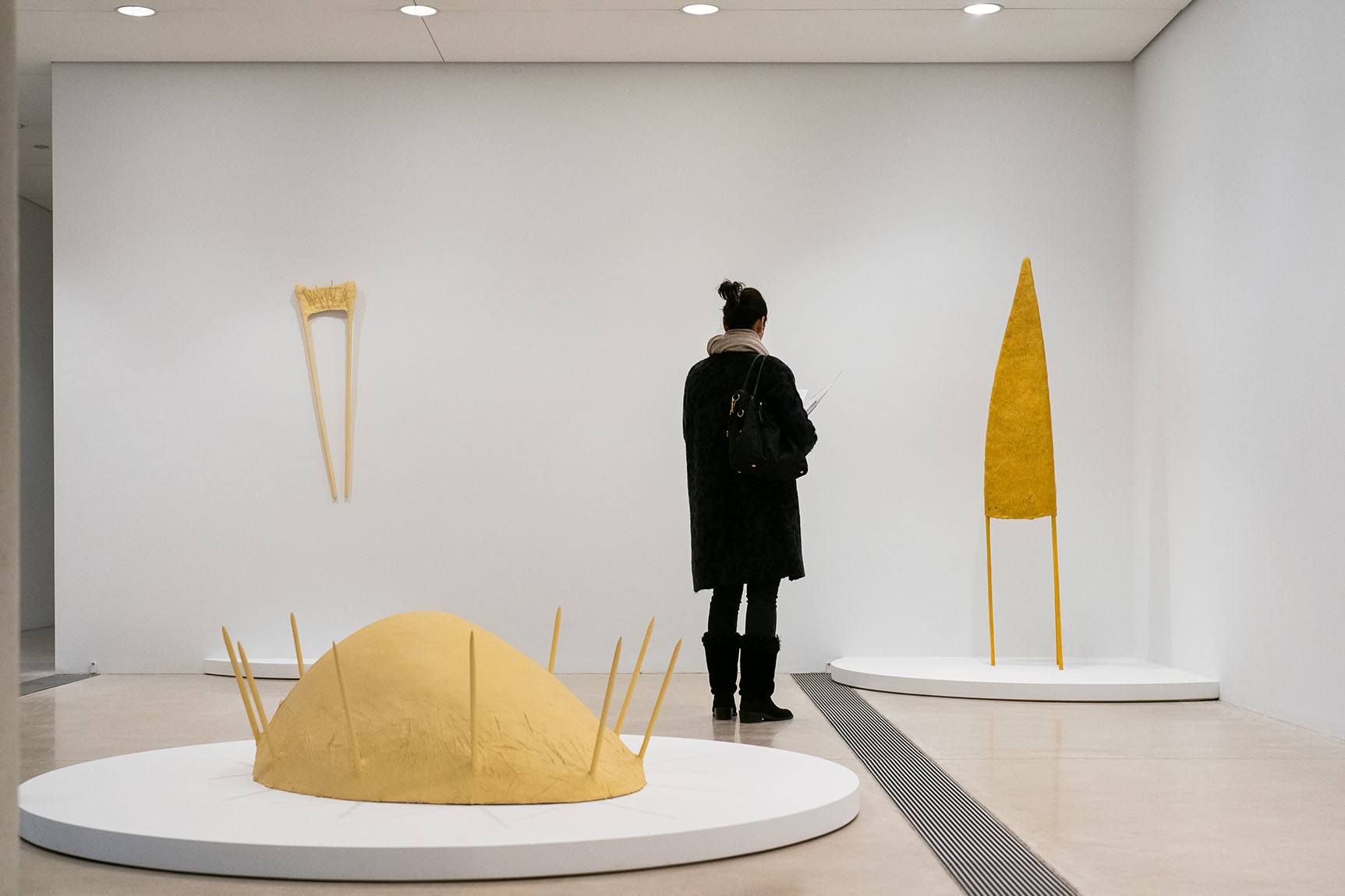 Person looking at yellow cone shaped sculpture with 3 legs