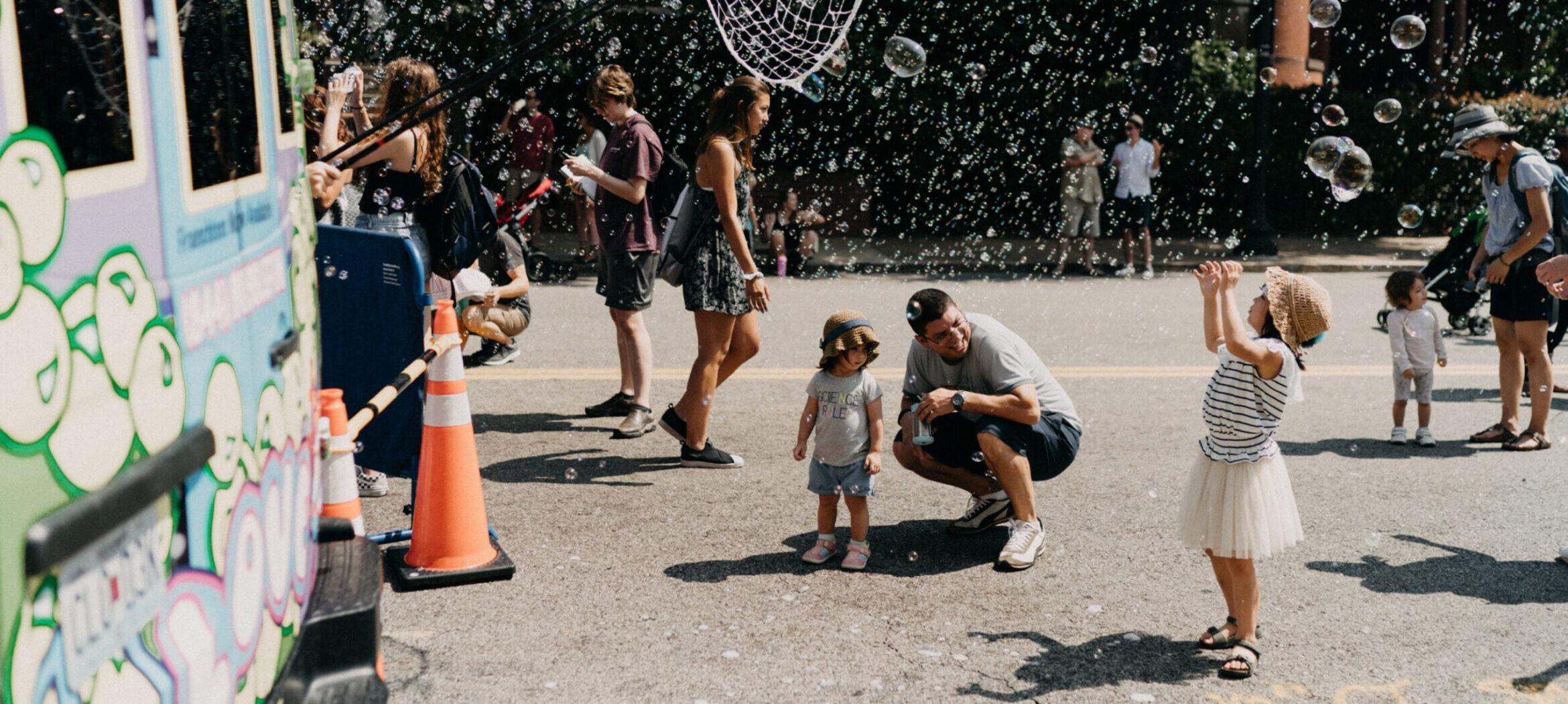 Little girl and family playing in bubbles from a bubble bus.