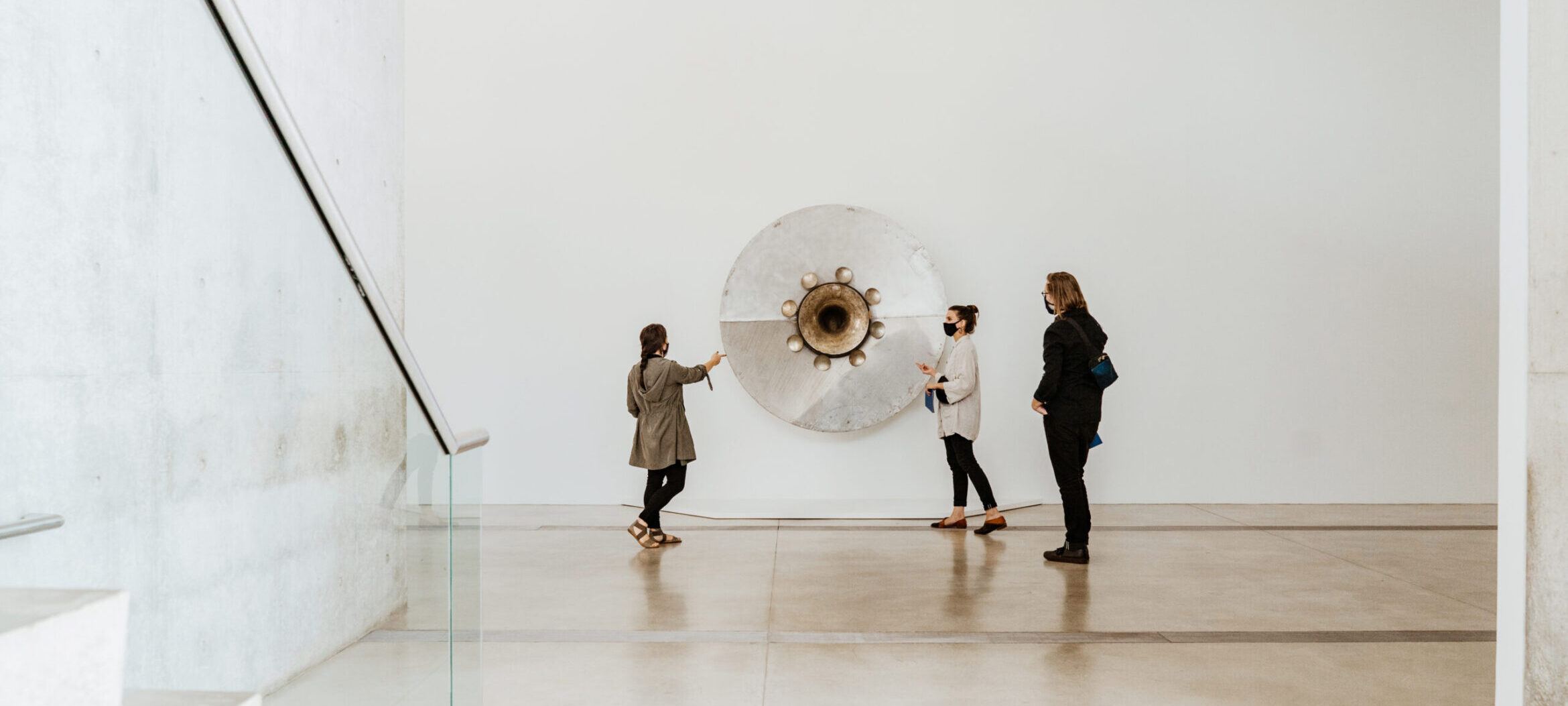 Three individuals looking at circular metallic sculpture from "Terry Adkins: Resounding."