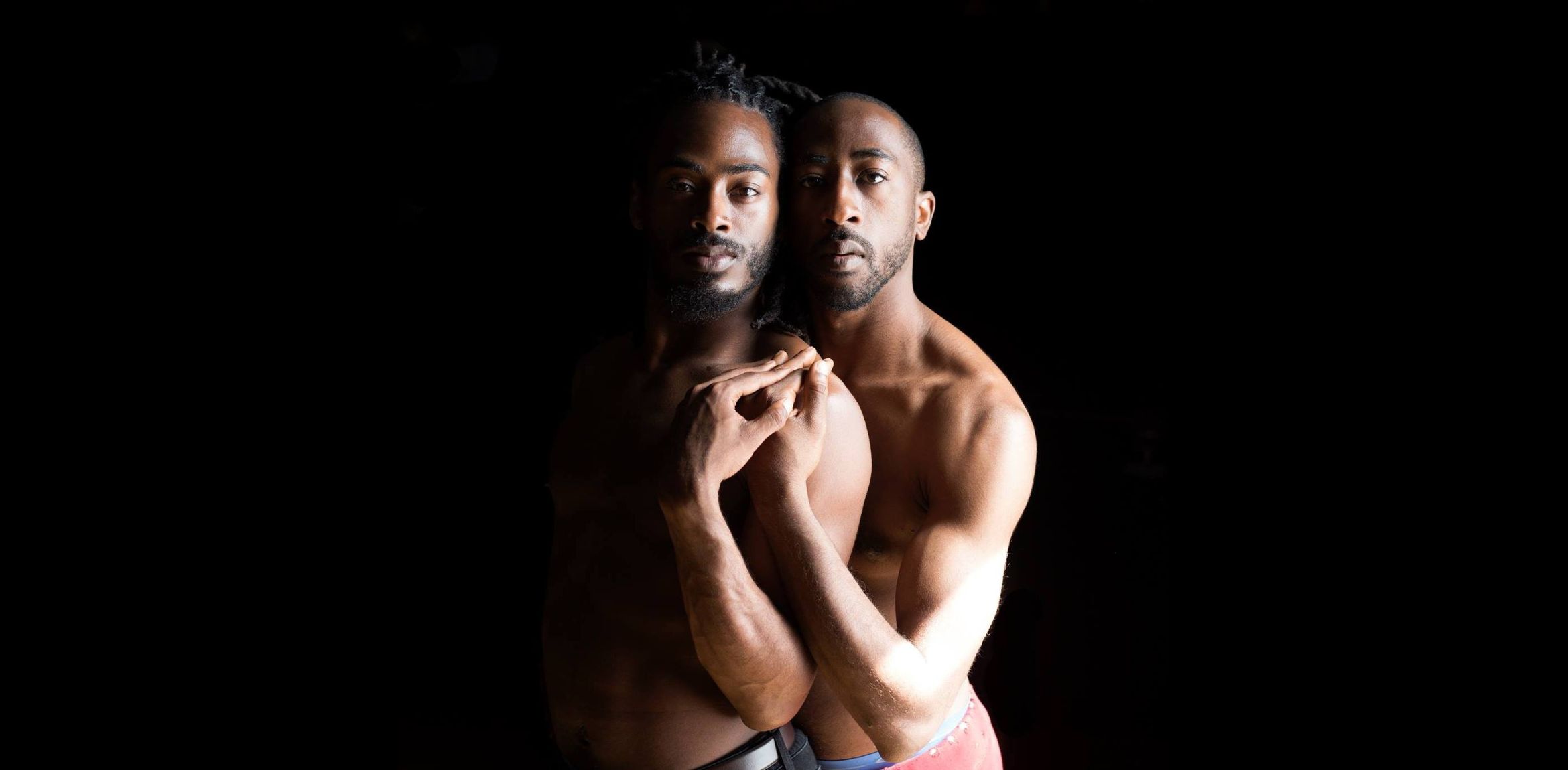 Two dancers posing together in a dark black background