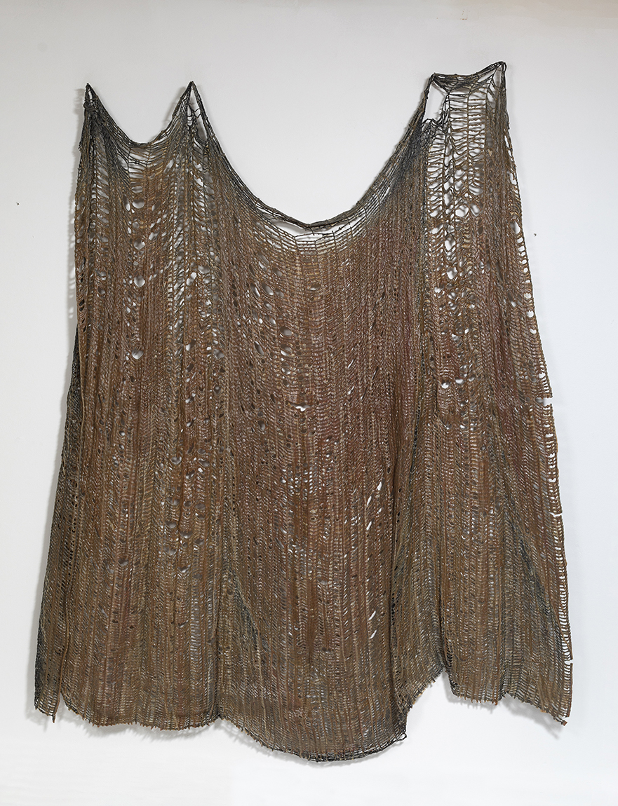 A muted brown distressed fabric-like acrylic on cotton thread resembling netting hanging on a white gallery wall